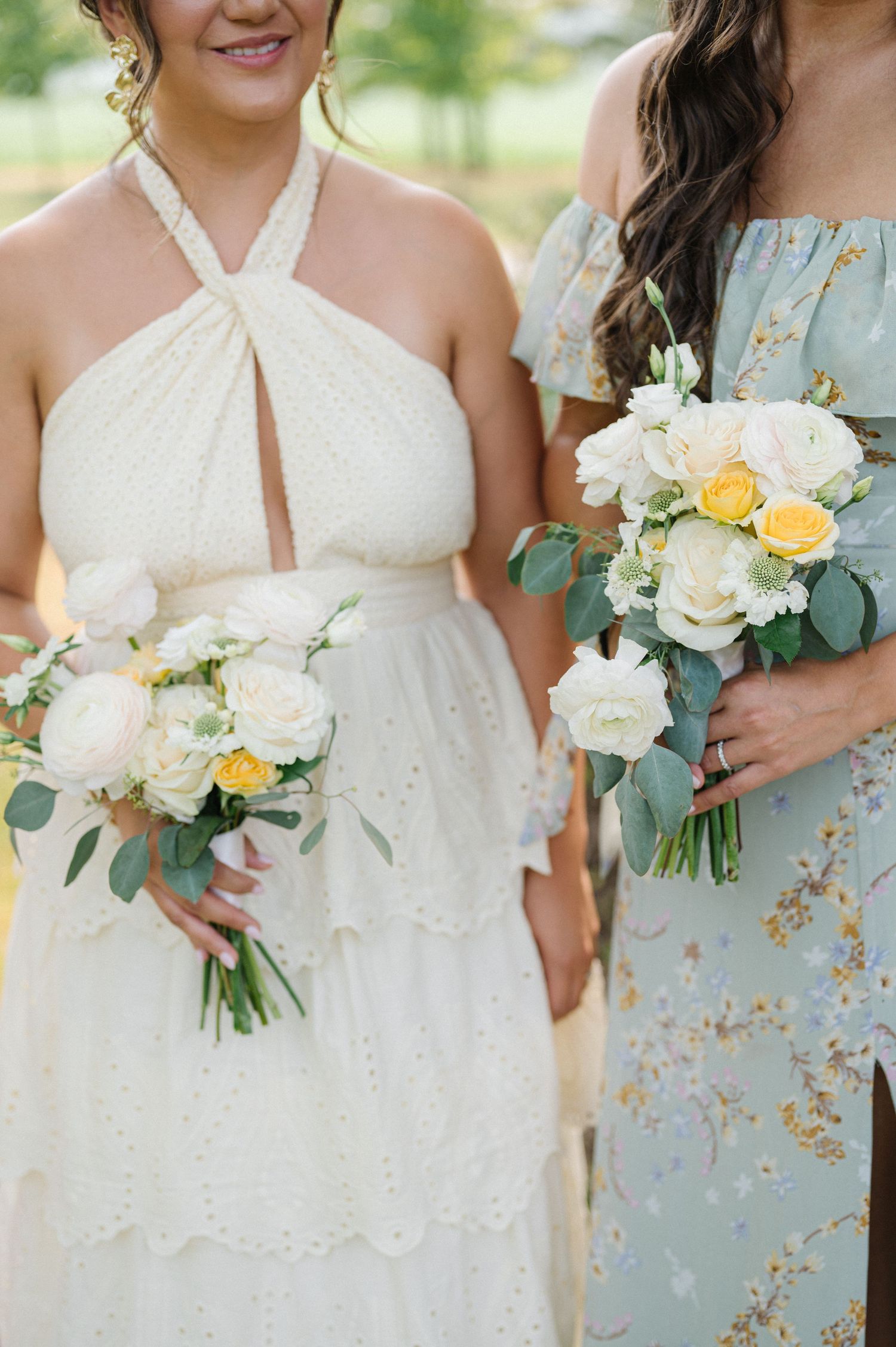 Bridesmaids holding matching bouquets of white and yellow roses with eucalyptus in white and light blue floral dresses.