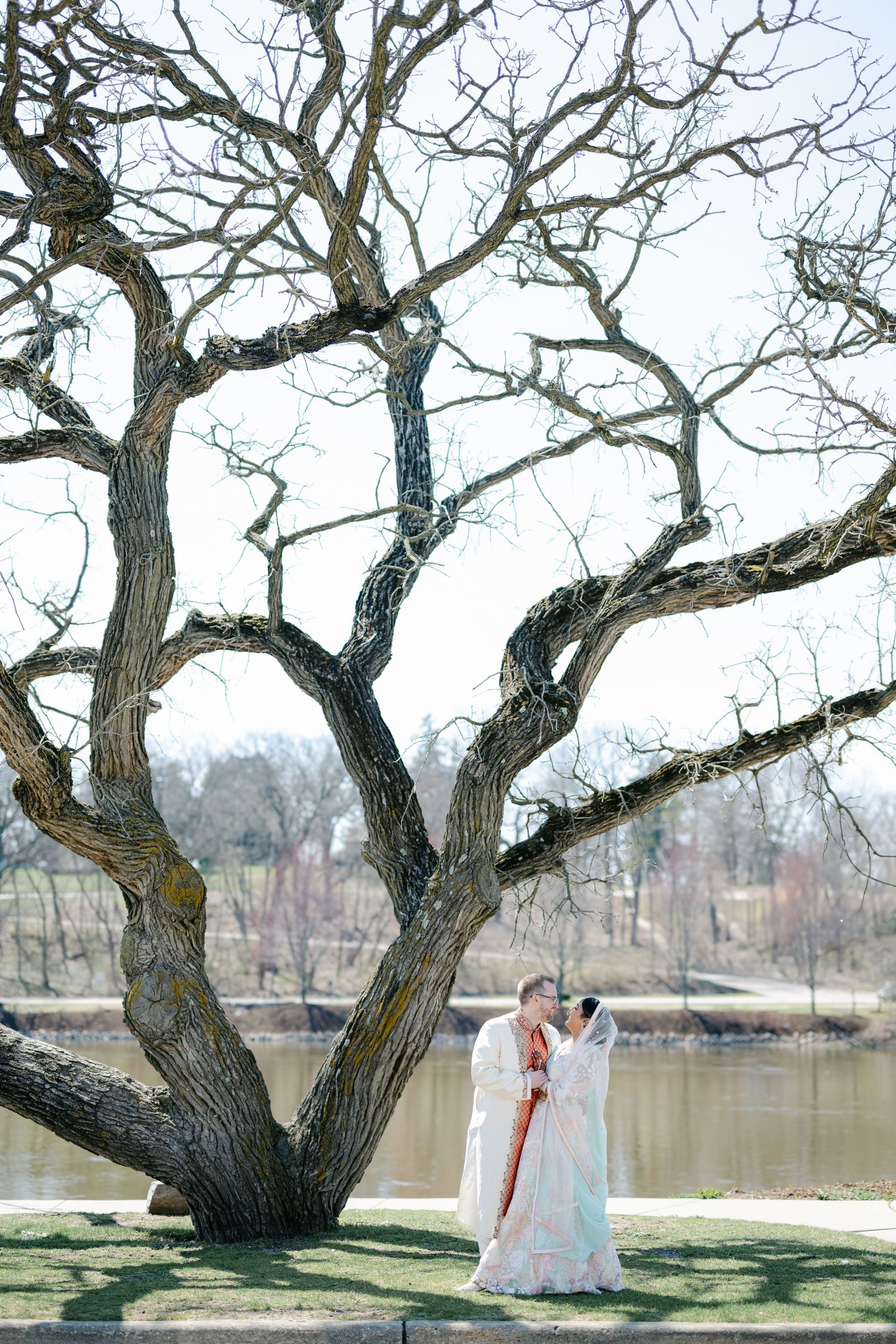 Two figures in white dresses stand beneath a twisted old tree by a tranquil lake on a spring day. - The Brix on the Fox