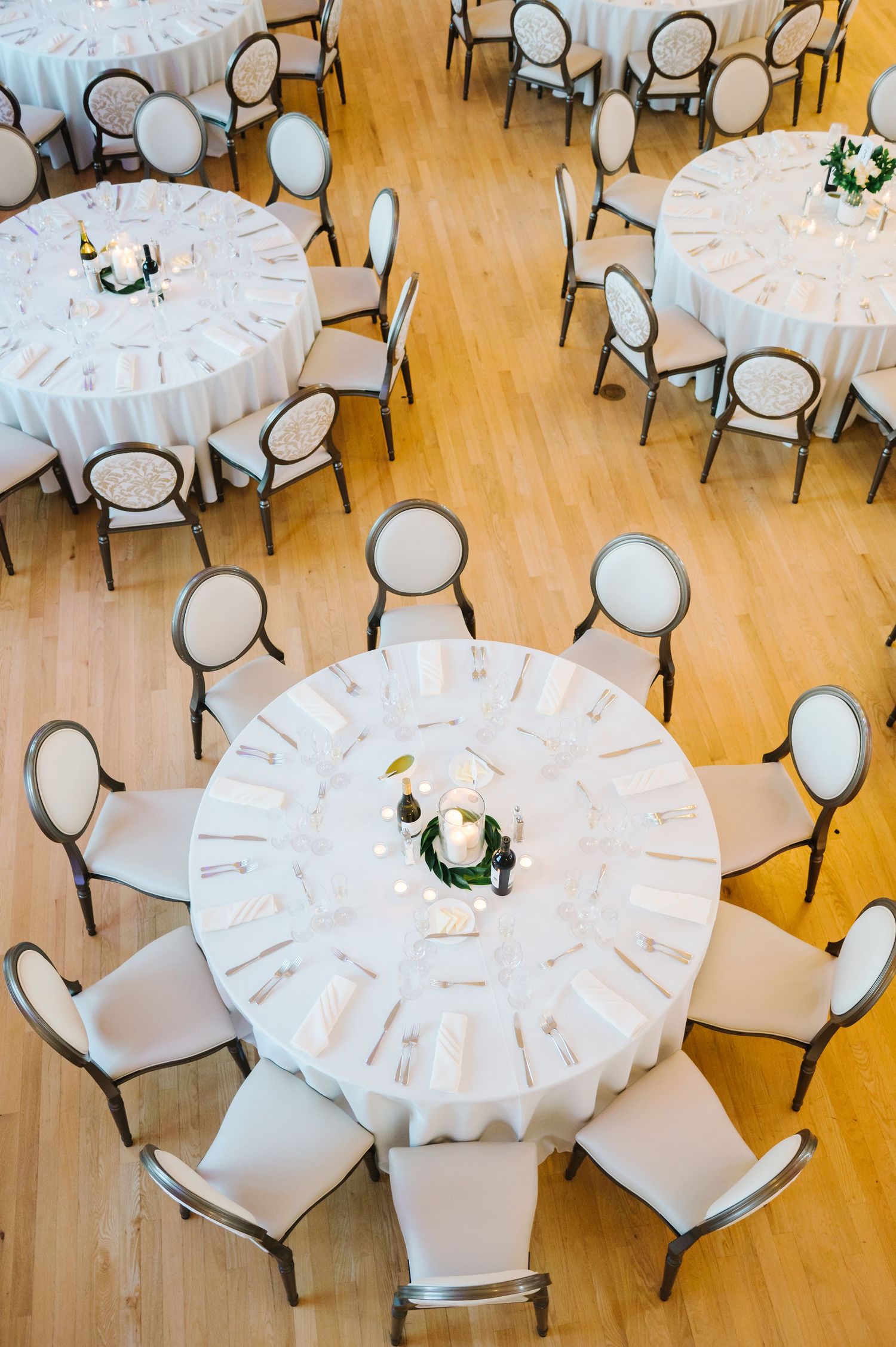 Elegant round banquet tables with white tablecloths and chairs arranged in a spacious room with hardwood flooring.