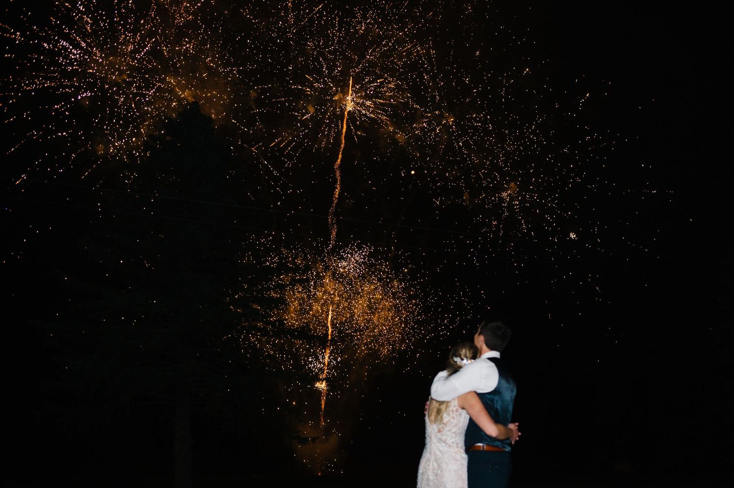 A couple dances under a dark sky illuminated by bursting fireworks creating a romantic nighttime celebration scene. - Heritage Prairie Farm