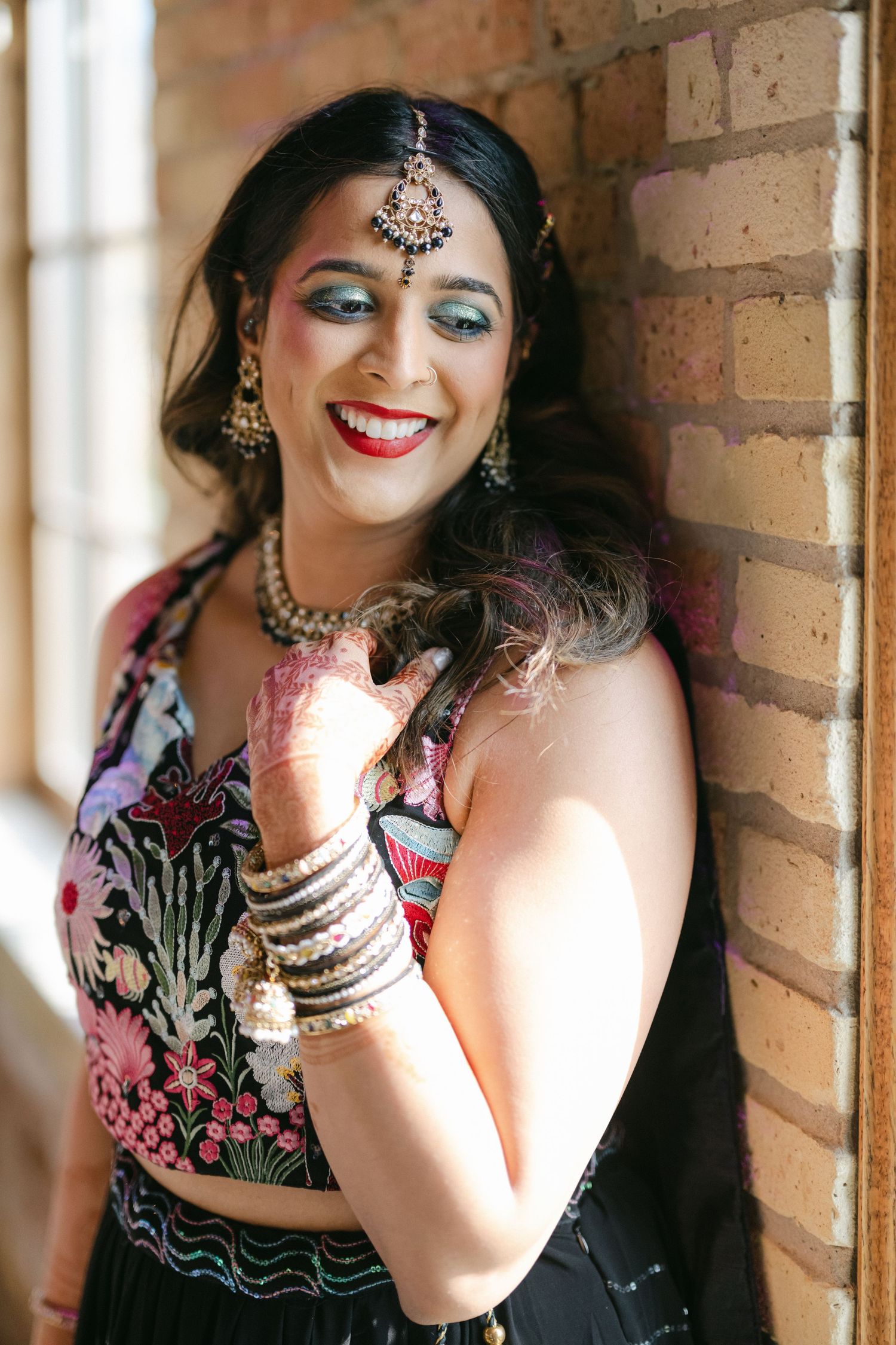 A woman in traditional Indian attire and jewelry poses against a brick wall in a portrait series. - The Brix on the Fox