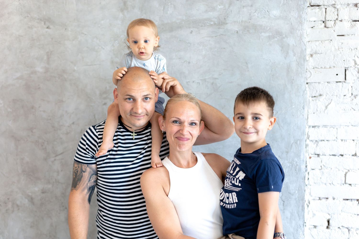 Indoor family portrait session with white brick backdrop and casual navy outfits.