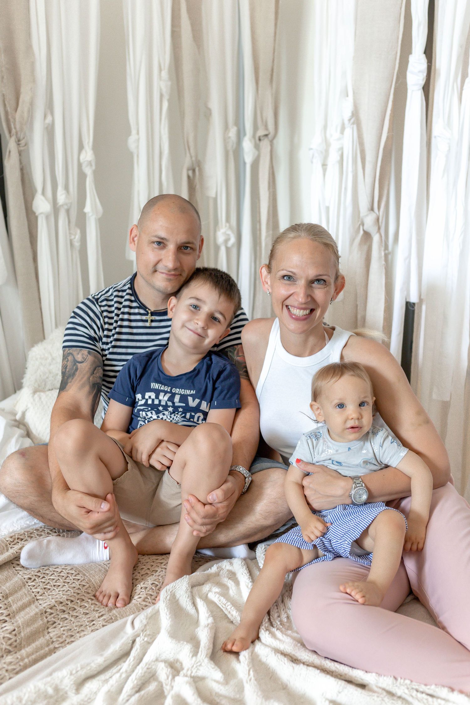 Relaxed family photo session on floor with white curtain backdrop.