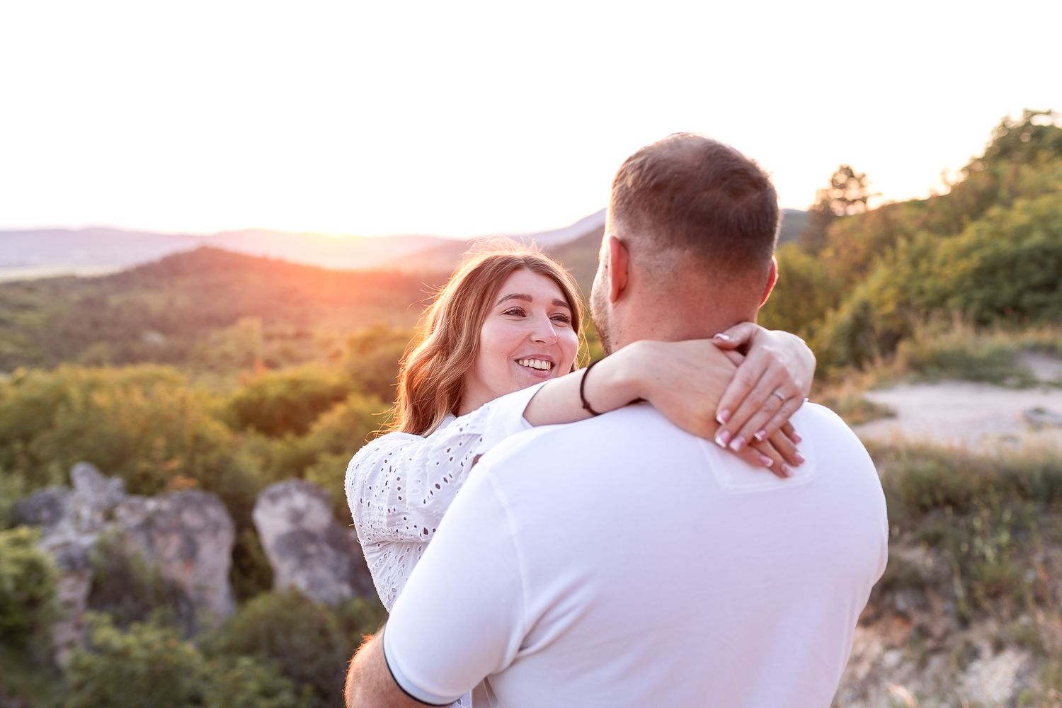 A romantic couple embraces while watching the sunset from a scenic mountain overlook.