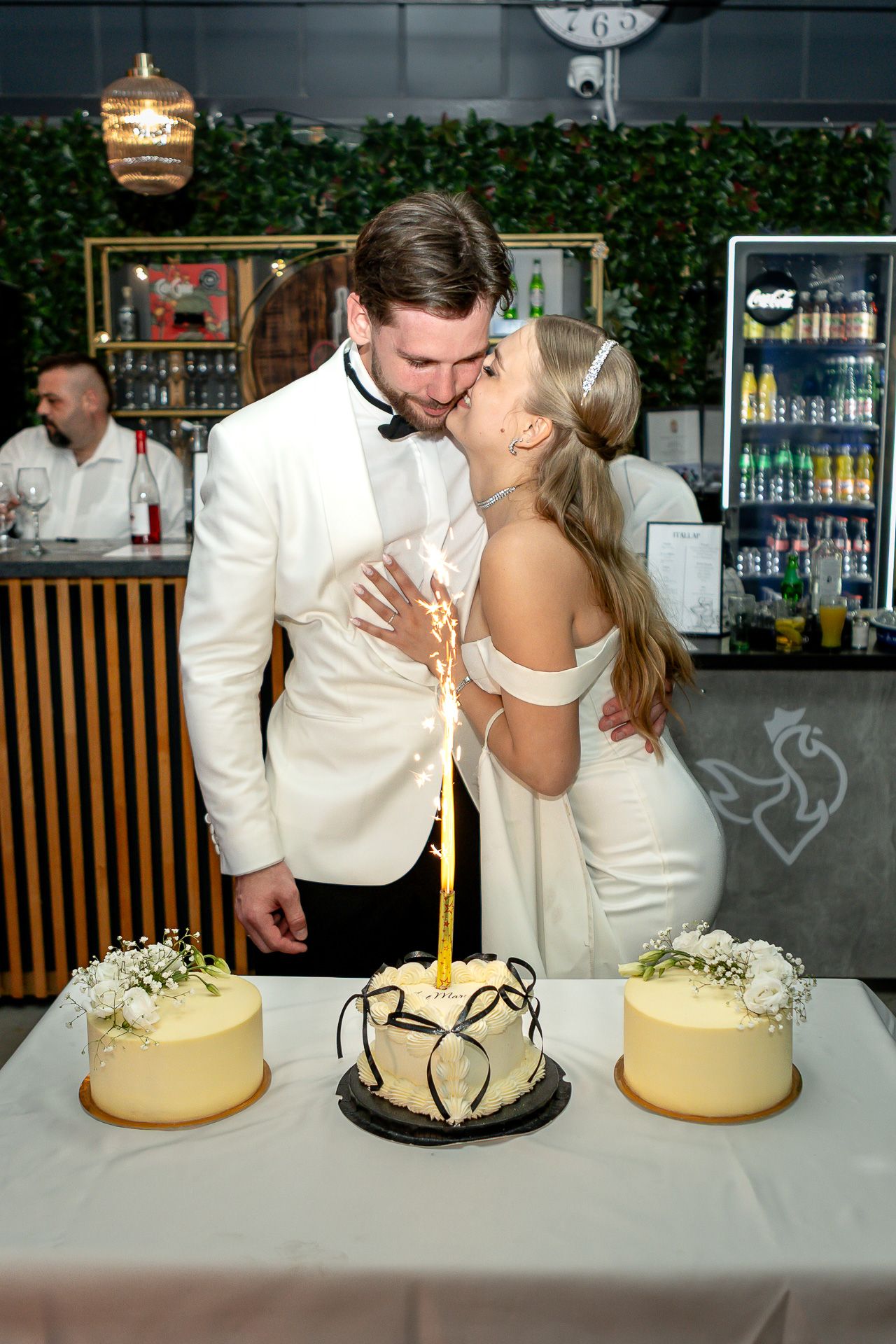 Three elegant wedding cakes displayed on a white tablecloth at a reception venue.