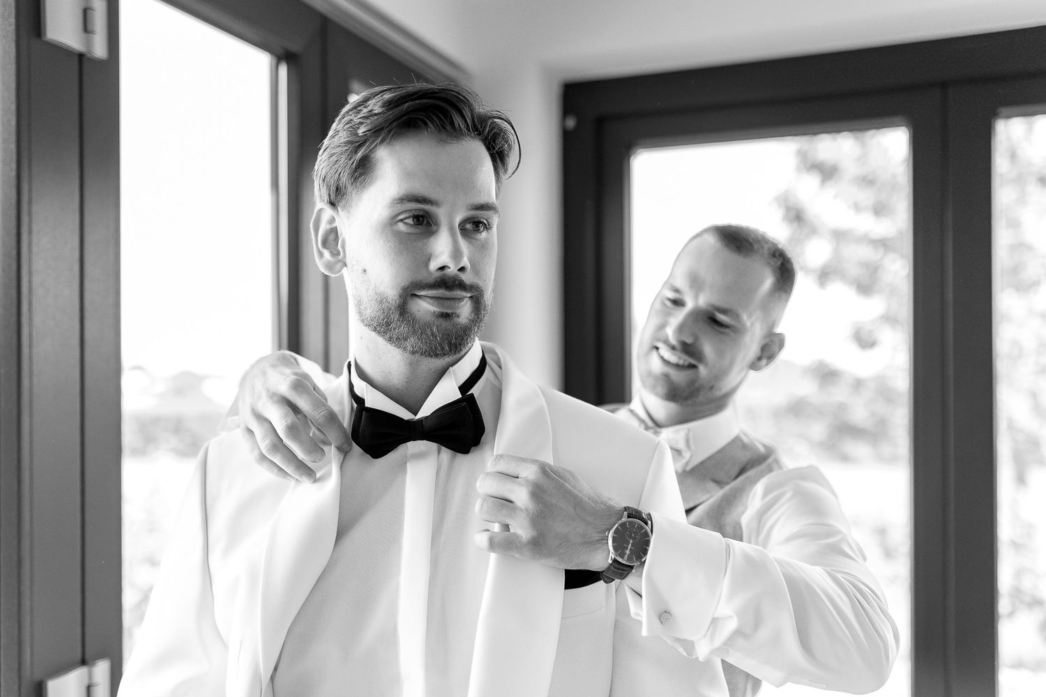 Wedding preparation moments captured in black and white showing formal attire adjustments.