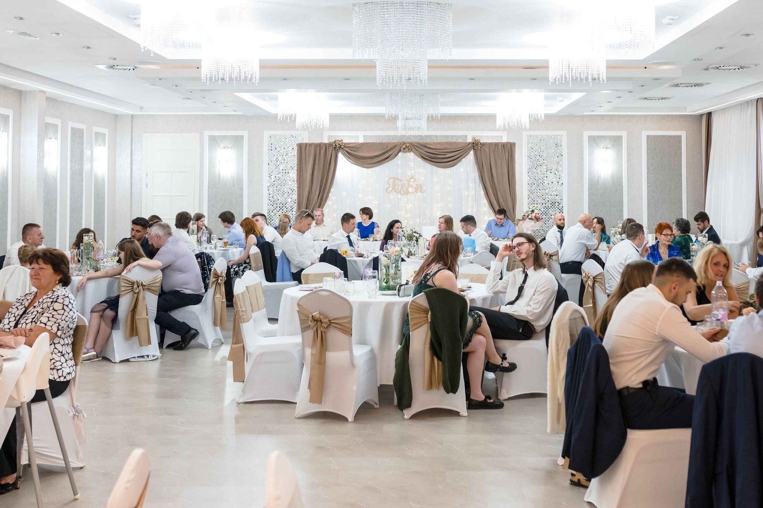 A panoramic view of an elegant white wedding venue with guests seated at tables during a reception celebration.