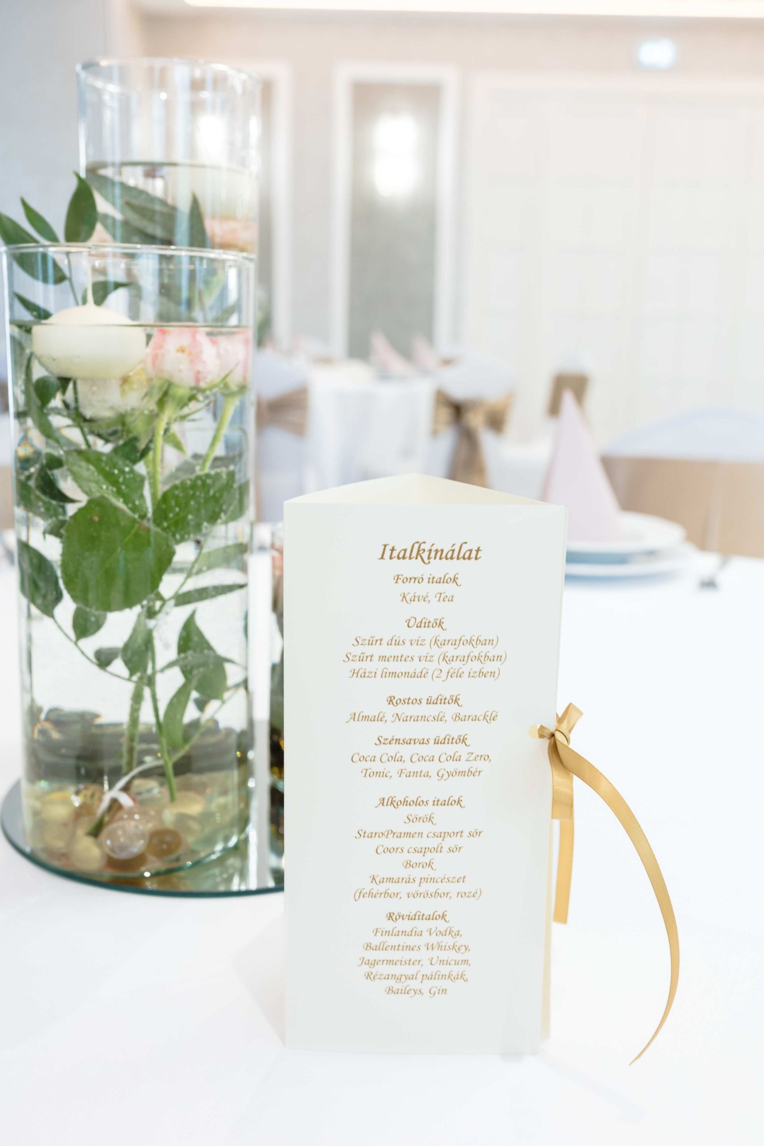Elegant wedding menu cards displayed next to glass vases with white floral arrangements in a bright modern setting.