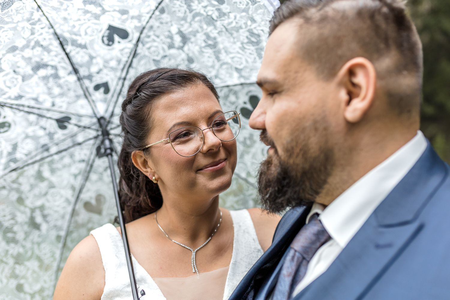 A couple in formal wedding attire shares an intimate moment together outdoors under blooming spring trees.