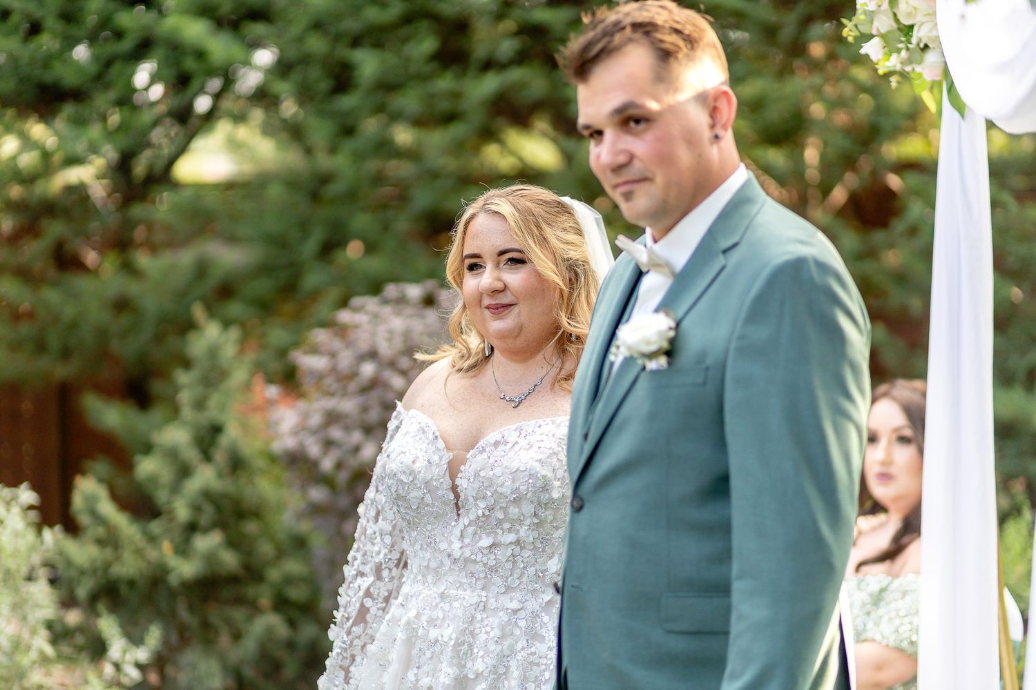 A couple shares a tender moment during their outdoor garden wedding ceremony beneath white pillars and greenery.