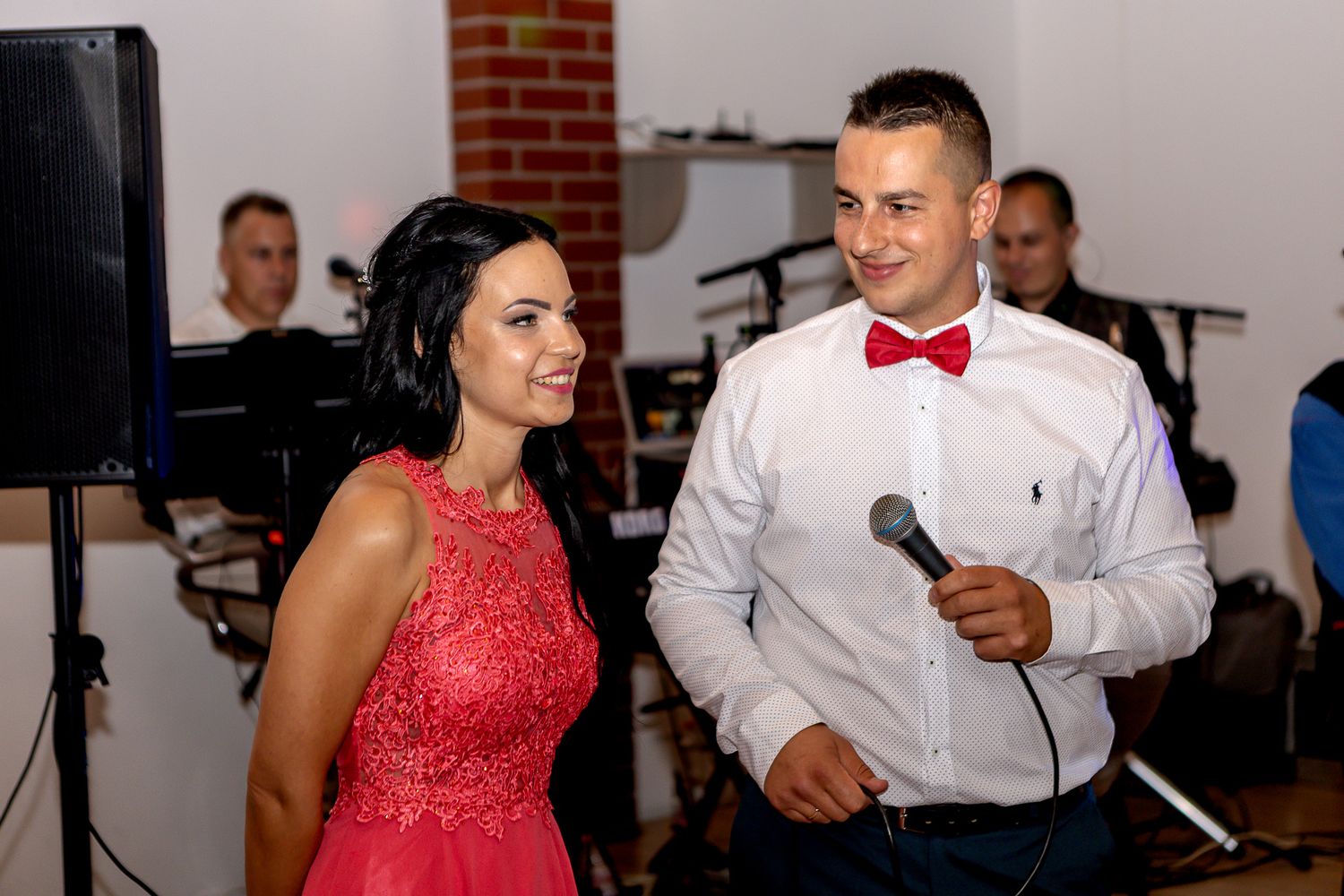 A couple in formal attire, with a red dress and white shirt, dancing together at an indoor event.