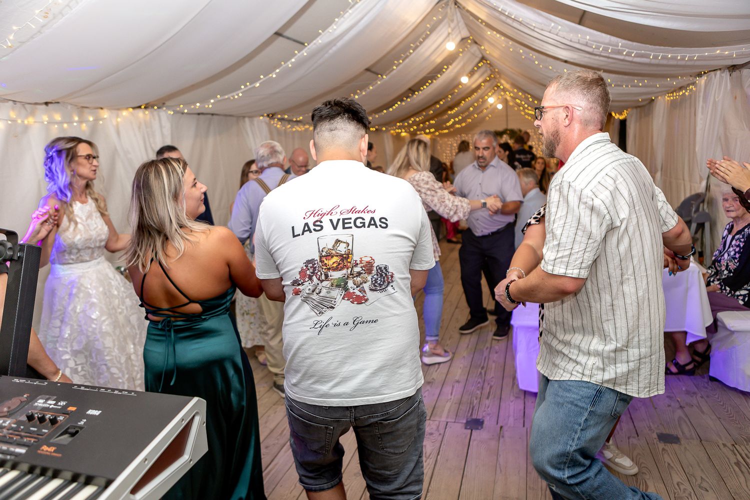 Wedding guests dance together on a decorated reception dance floor with string lights overhead.