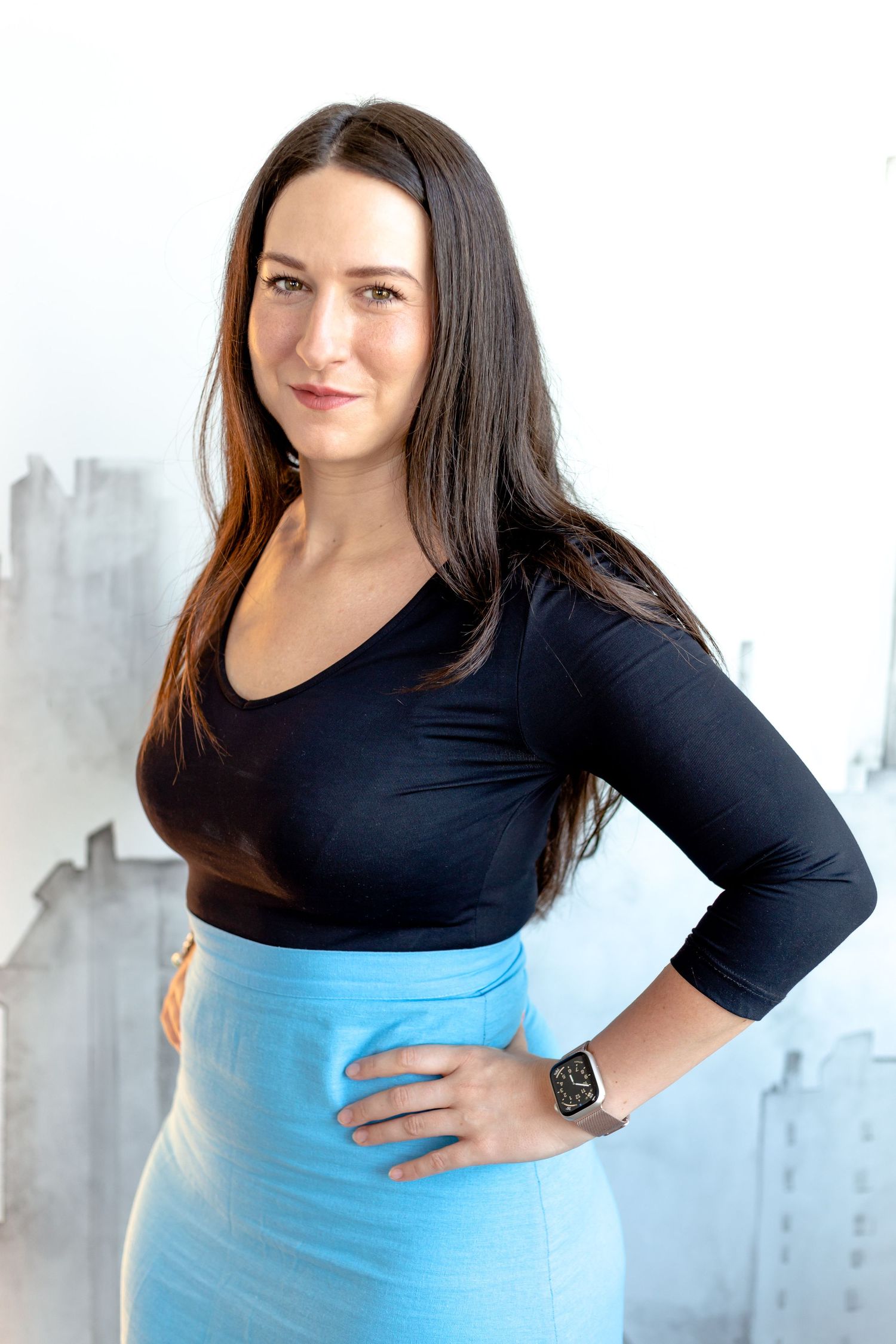 A person wearing a black long-sleeve top and blue skirt poses in a bright studio setting.