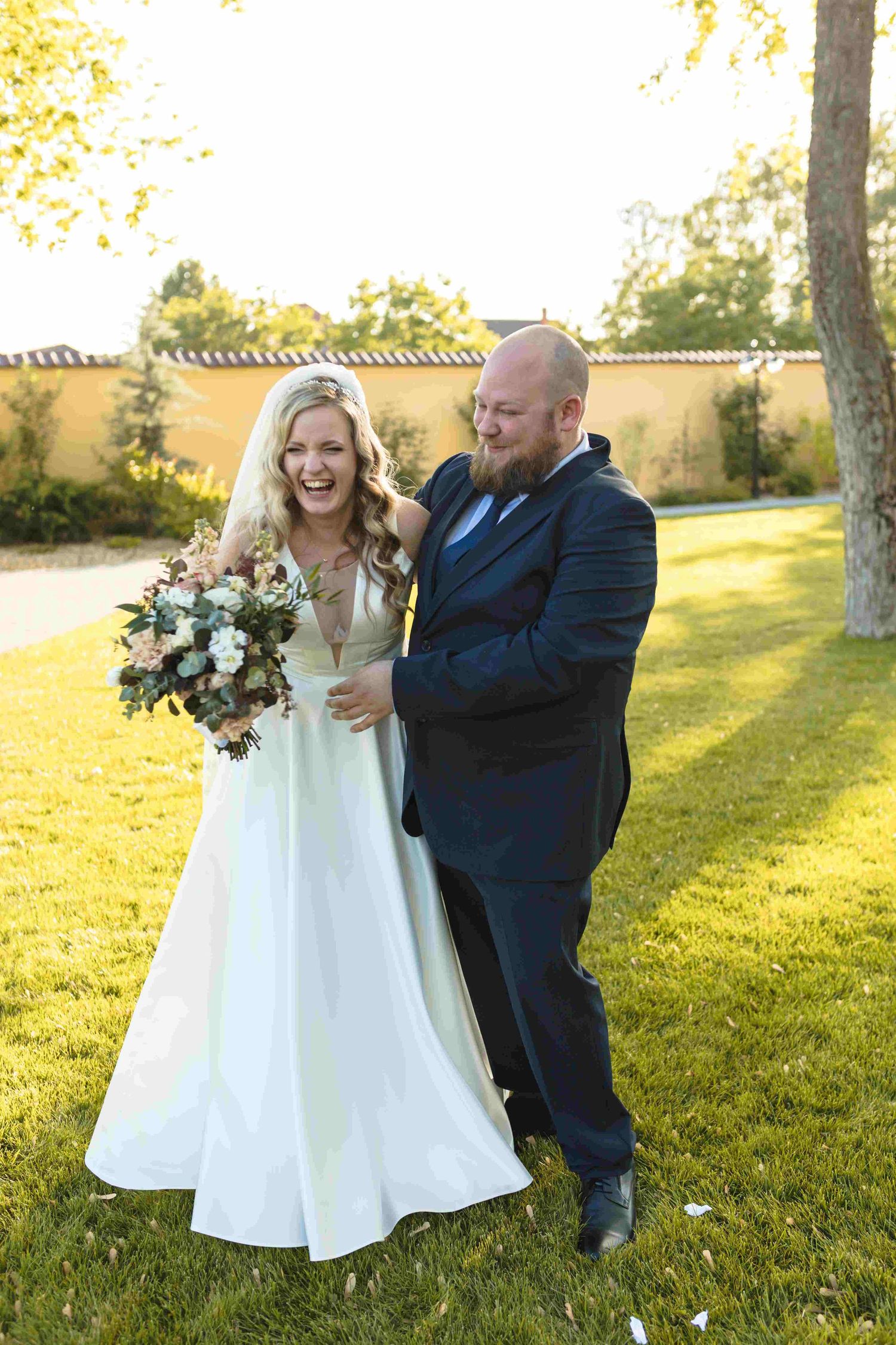 Joyful wedding couple shares candid moments in a sunlit garden setting with natural golden light.