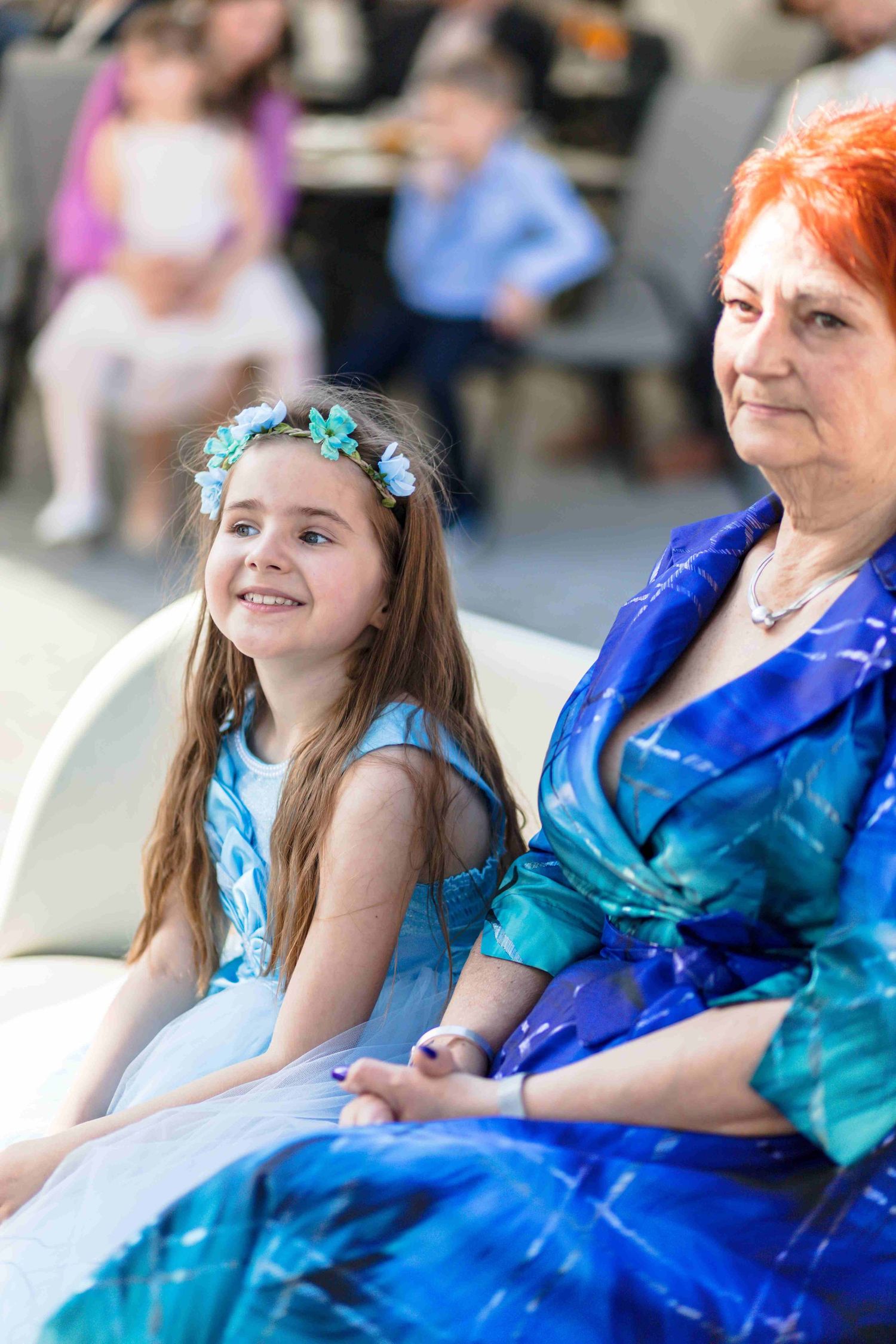 Two attendees in coordinating blue dresses sit together at a formal event.