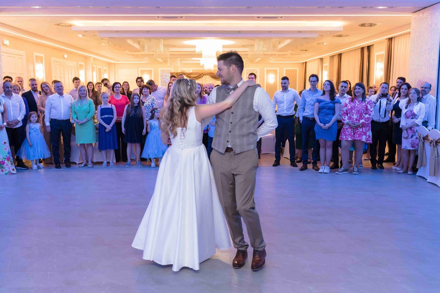 Wedding couple performs a choreographed dance routine on a ballroom floor surrounded by guests.