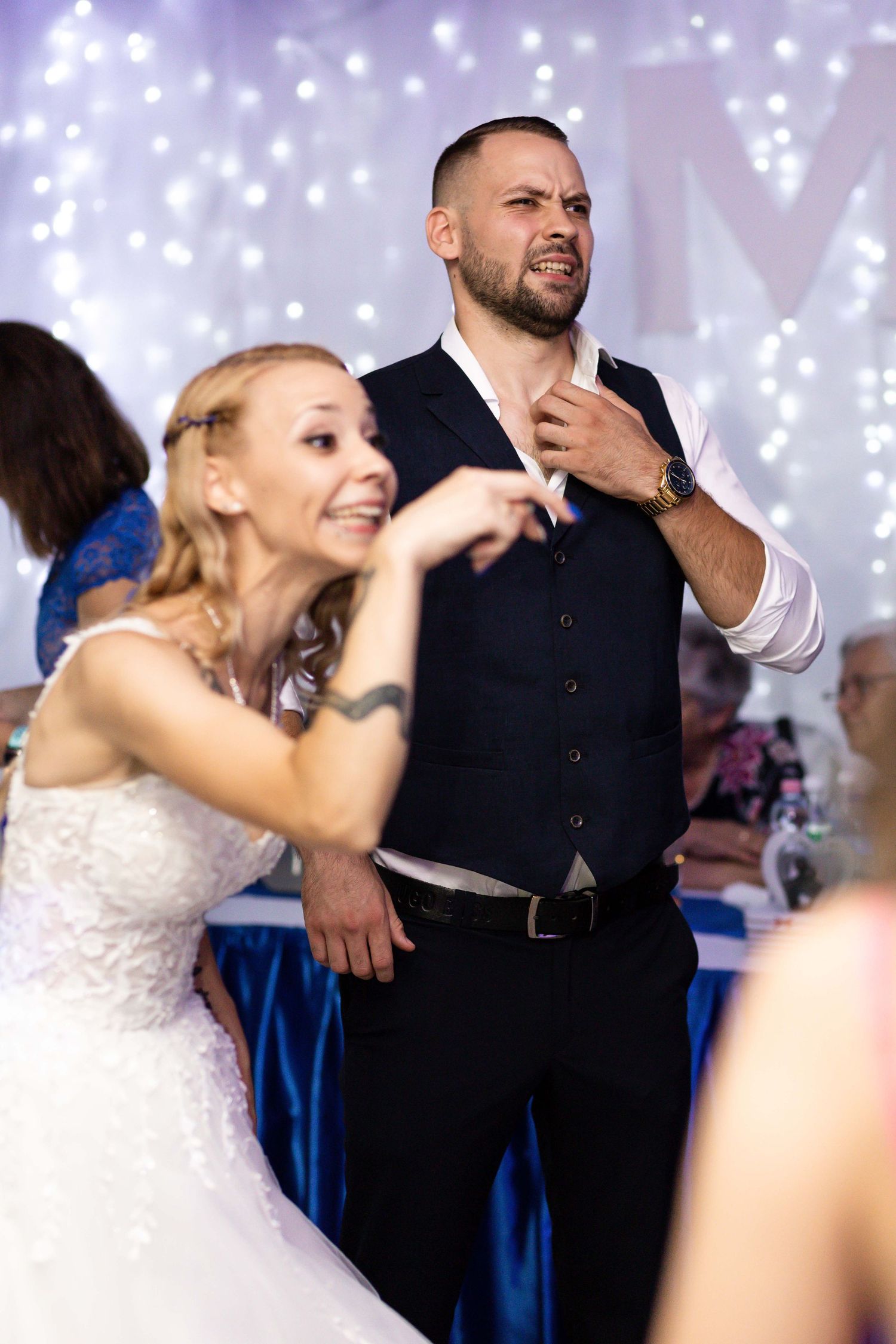 A bride and groomsman dance energetically together at a wedding reception with twinkling lights in the background.