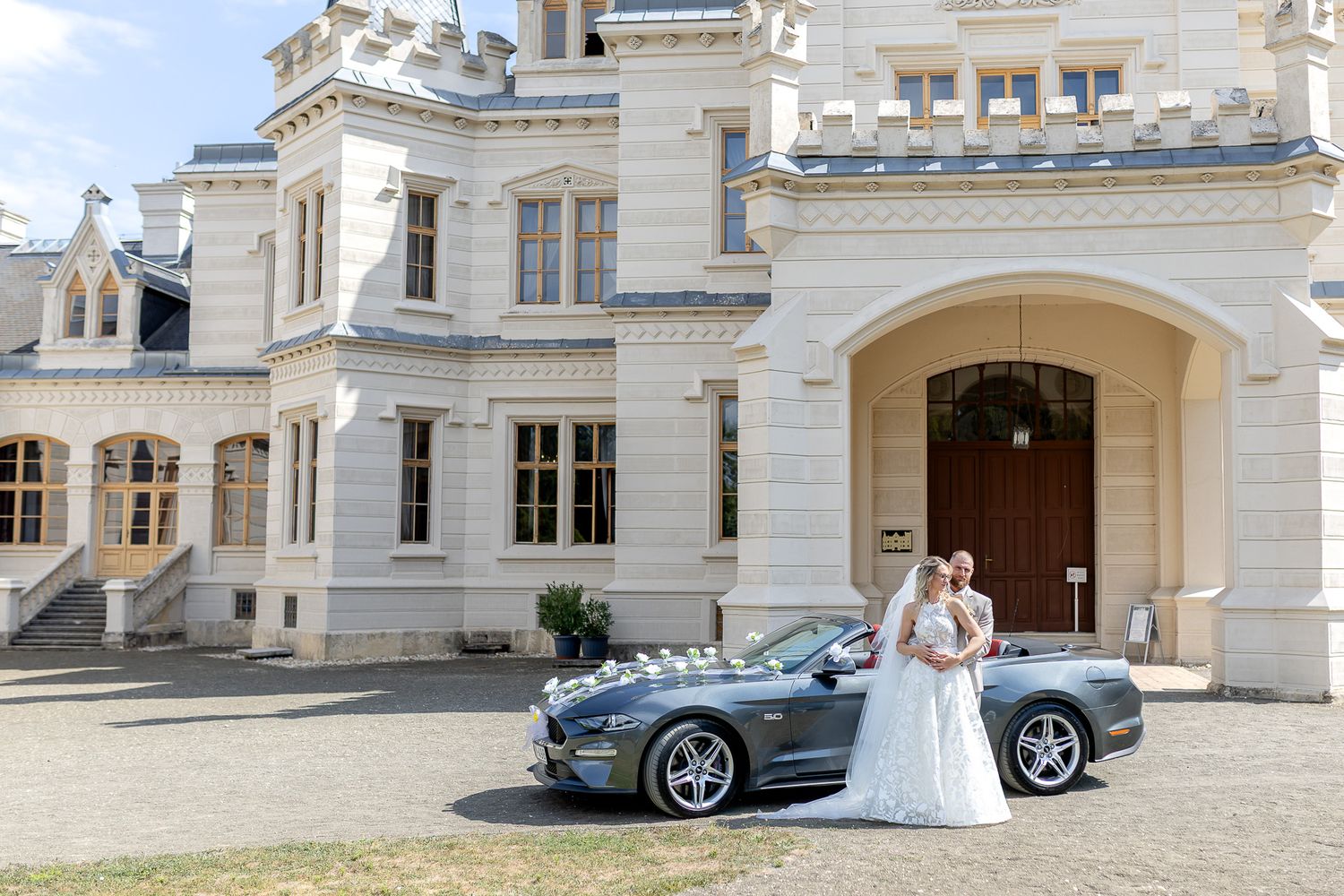 Luxury silver sports car parked in front of an elegant white stone mansion with classical architecture.