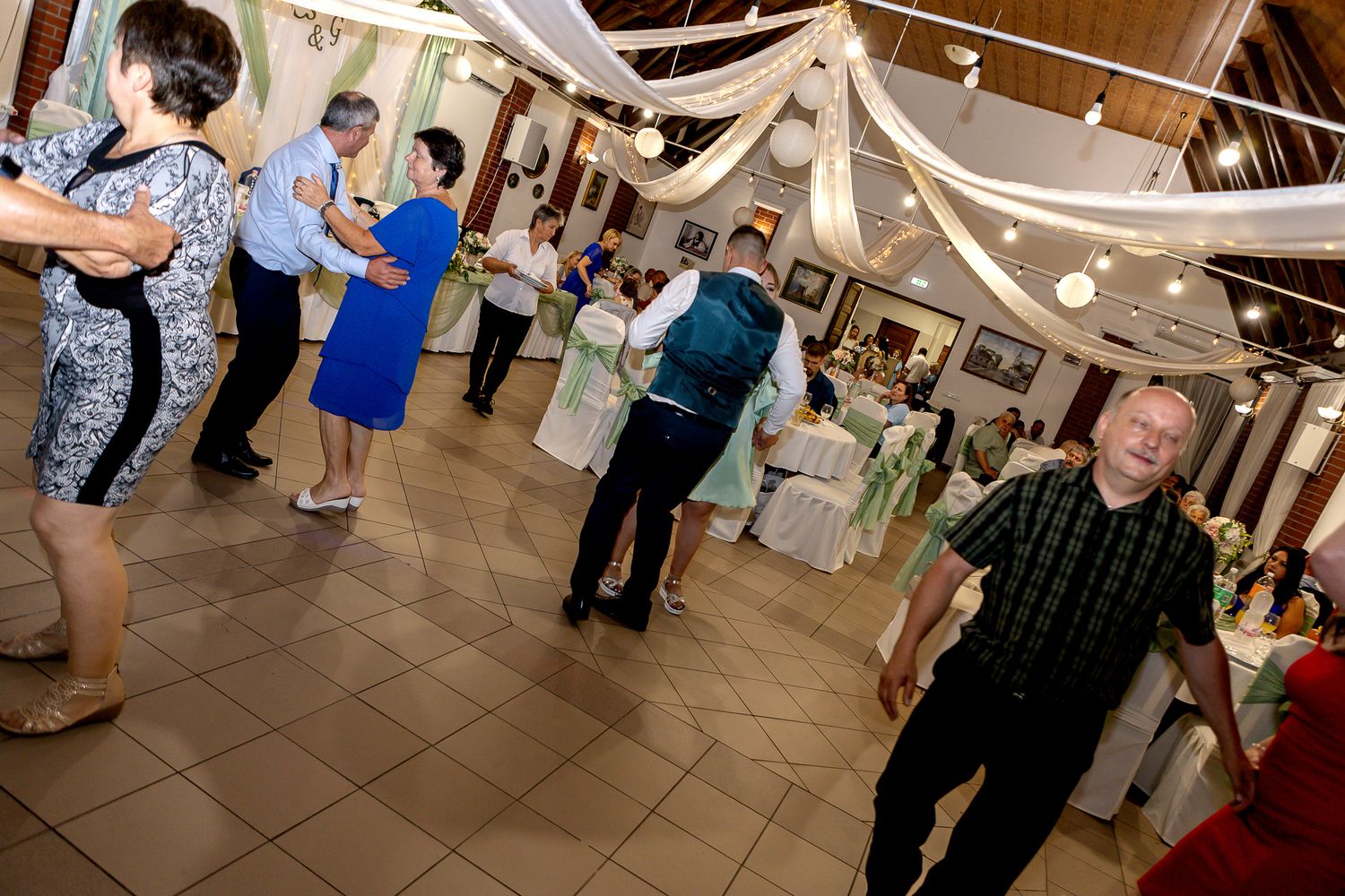 A group of people dancing together at an indoor event with decorative string lights overhead.