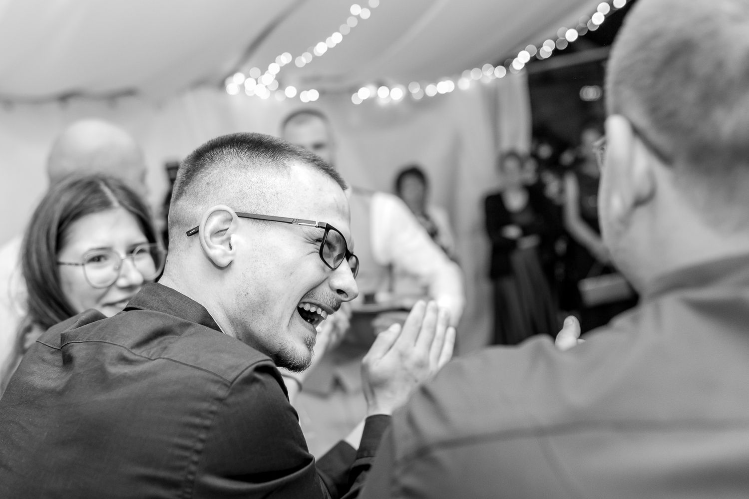 Black and white photo of couples slow dancing at an indoor wedding reception with twinkle lights.