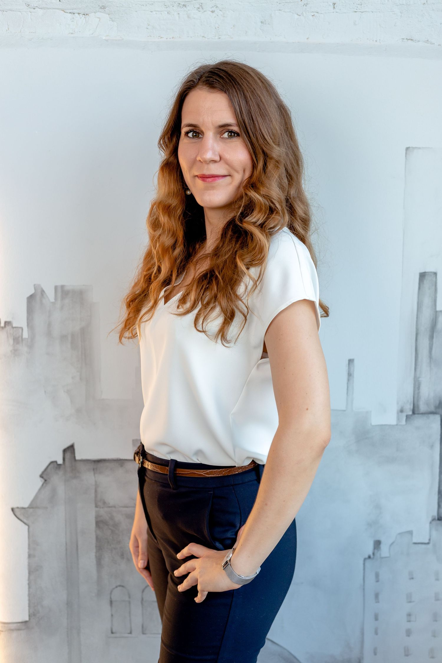 Professional portraits against abstract grey wall art wearing white blouse and navy pants.
