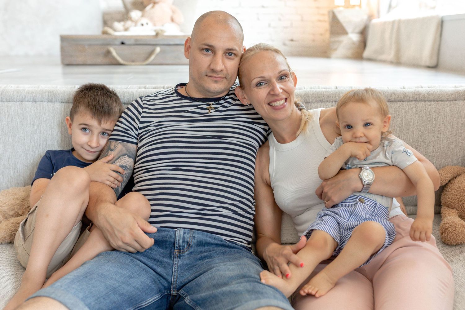 Family lying together on a white floor in casual clothing during an indoor photoshoot.