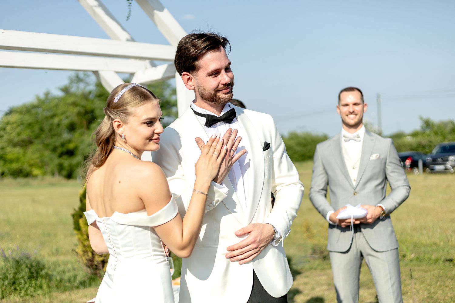 Elegant outdoor wedding celebration with couple and guests in formal attire on sunny day.