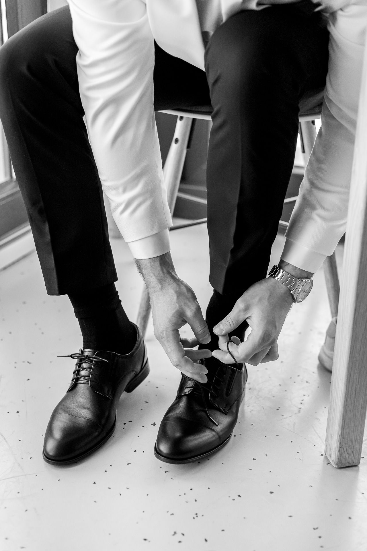 Black and white photo of formal shoes and pant legs during wedding preparations.