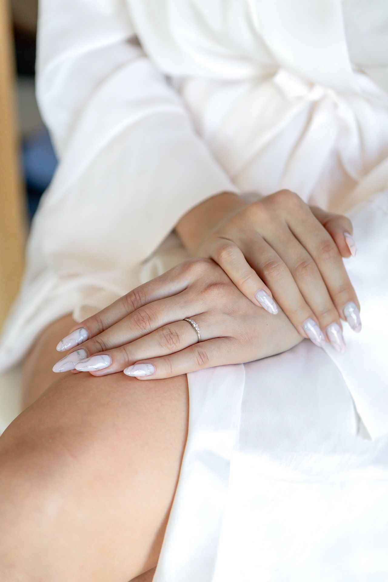 Hands with white manicure resting on leg wearing white clothing.