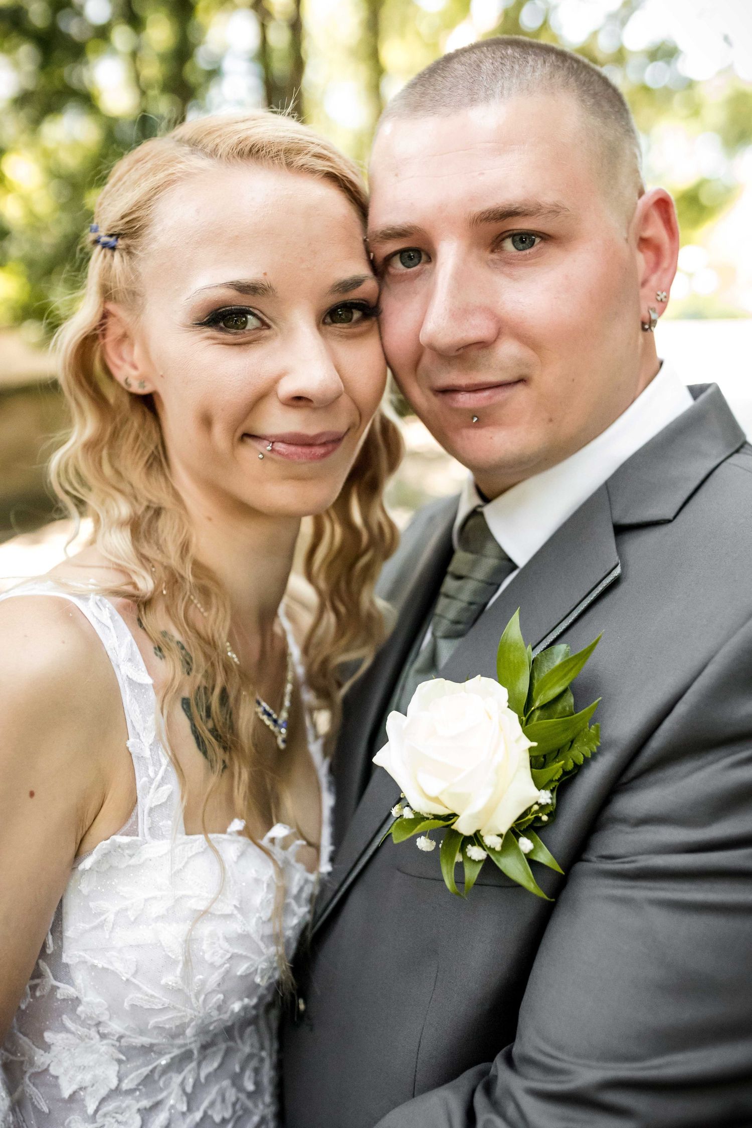 A close-up wedding portrait outdoors with a white rose boutonniere and natural bokeh background.