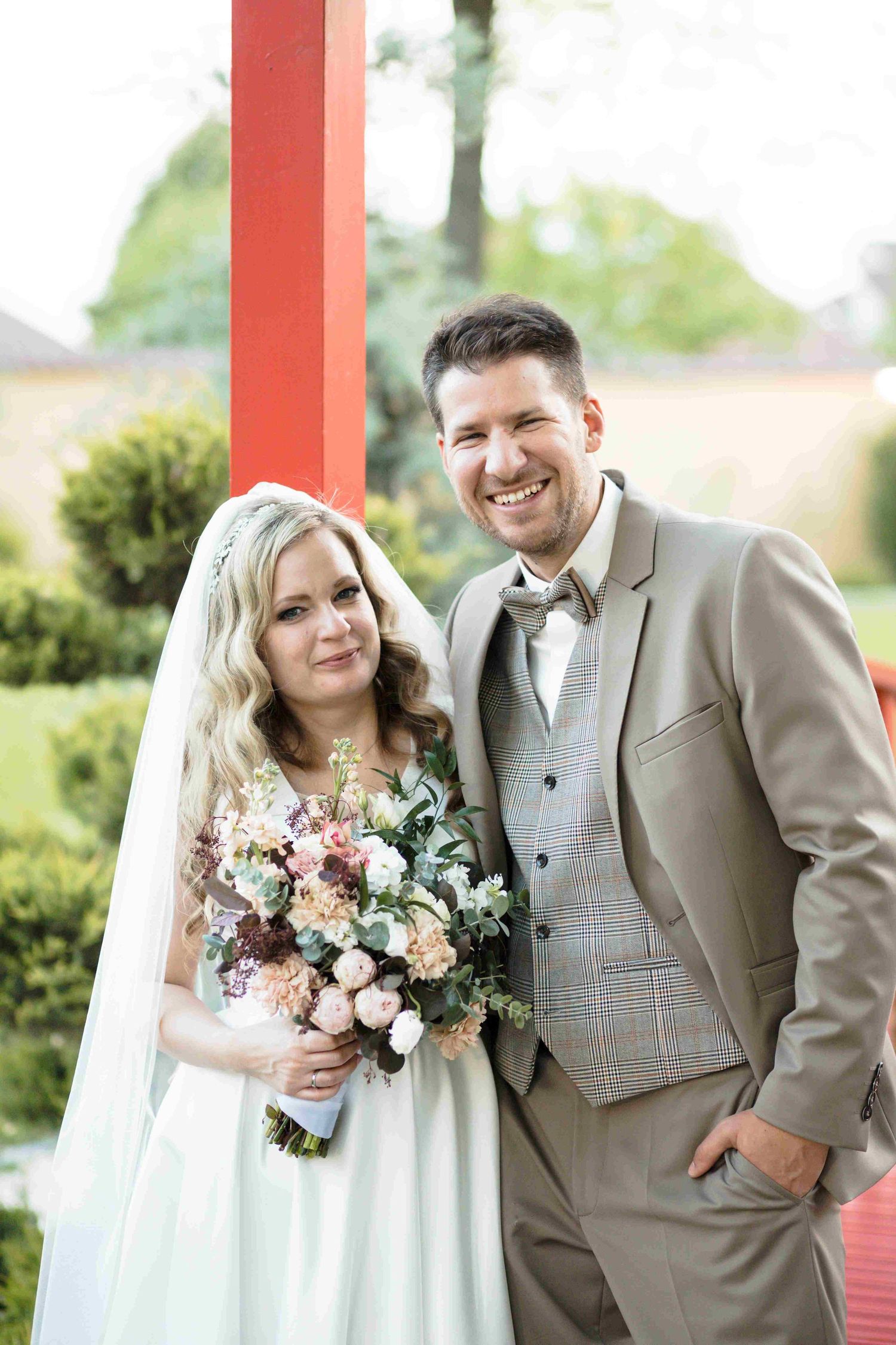 A happy couple poses together at their wedding, with the bride holding a beautiful pink and white floral bouquet.