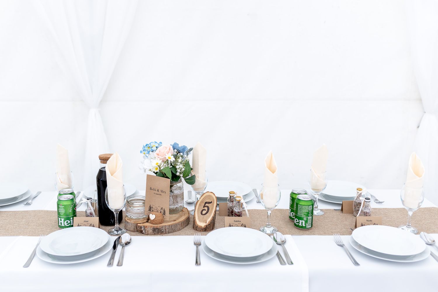 A rustic dining table setting with white plates, burlap runner, and glass bottles arranged for a casual gathering.