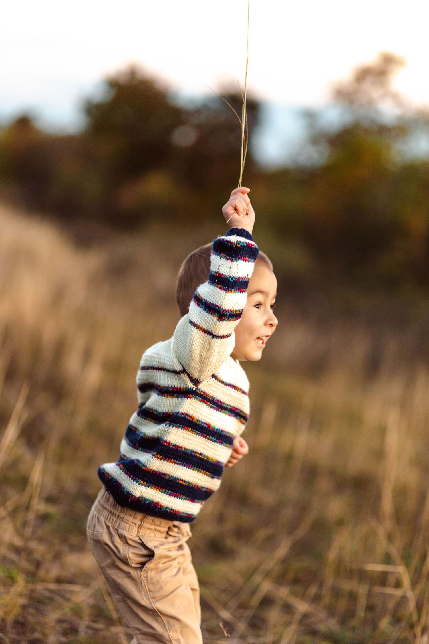 Child playing in tall grass during sunset wearing striped sweater.