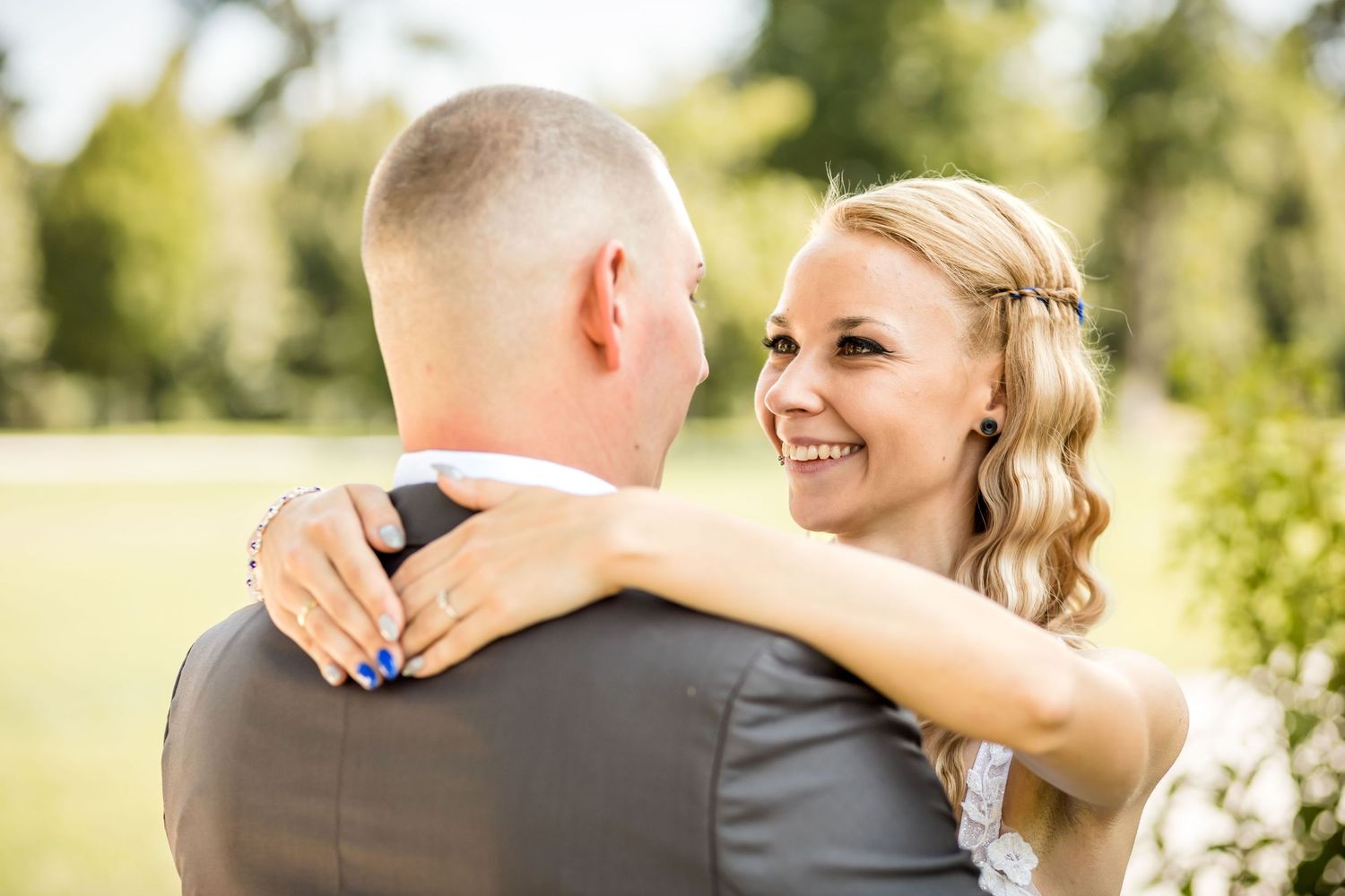 A couple shares a joyful moment together in a sunny outdoor setting with natural greenery in the background.