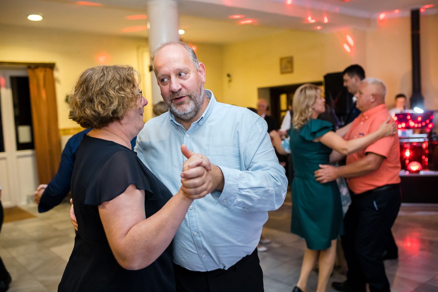 People dancing together in pairs at a social gathering with warm lighting and a festive atmosphere.