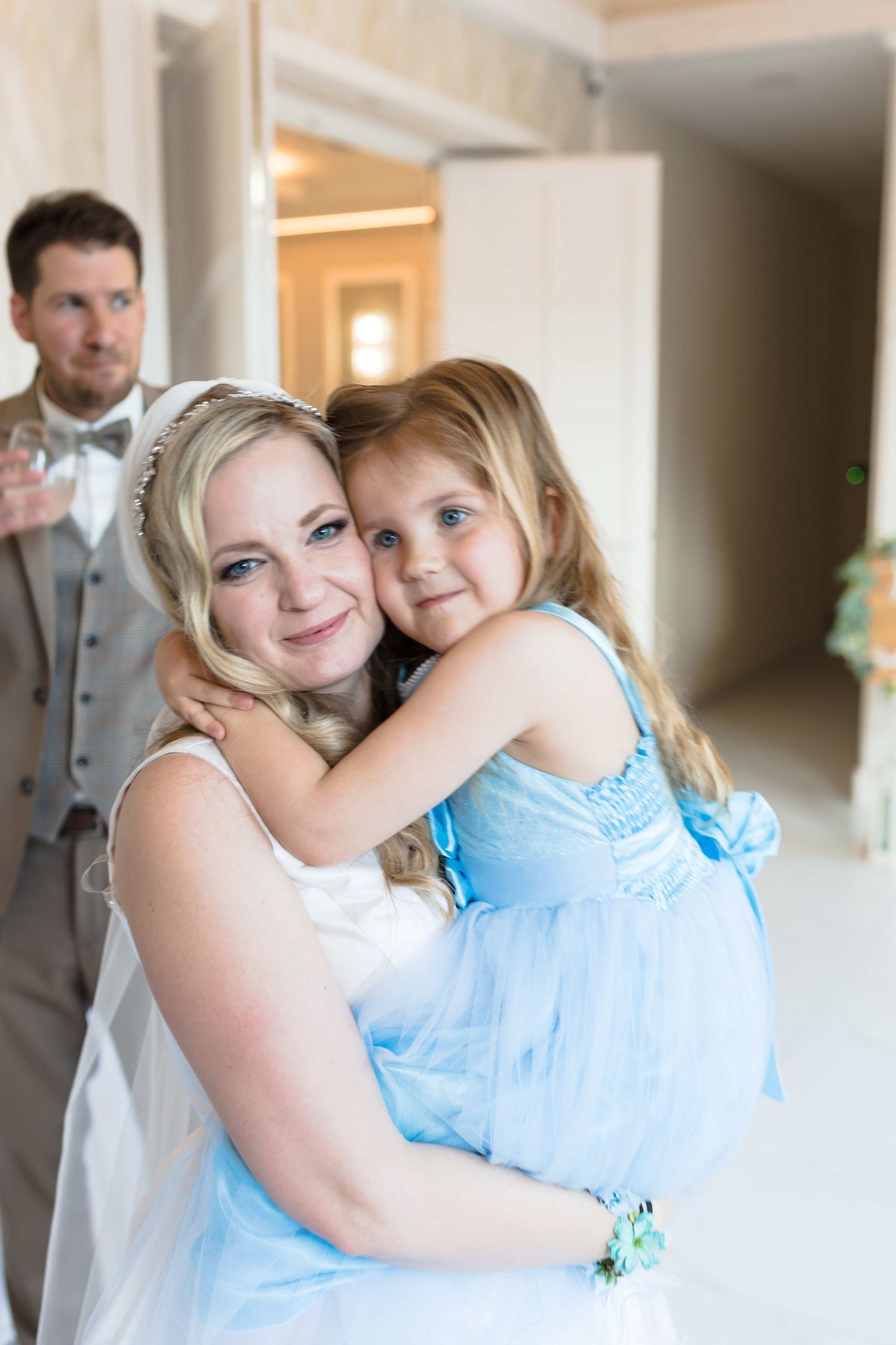 A tender moment shared between a bride in white and a young girl in a light blue dress at a wedding celebration.