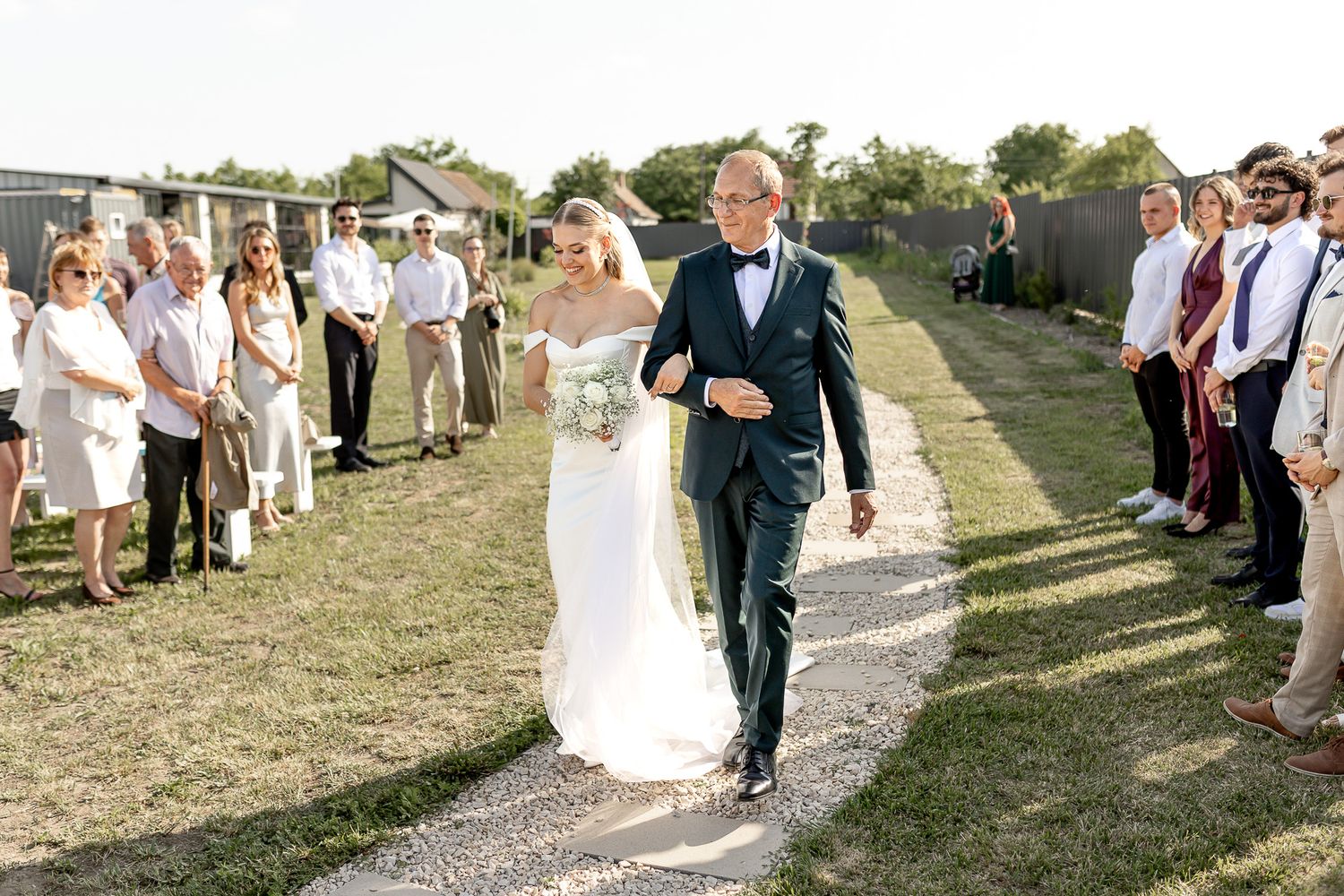 Wedding party processes down outdoor path with guests lined up on both sides.