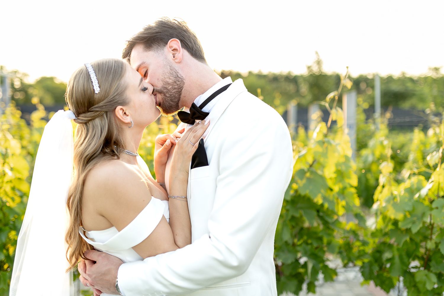 Newlyweds share intimate moments among vineyard rows at sunset.