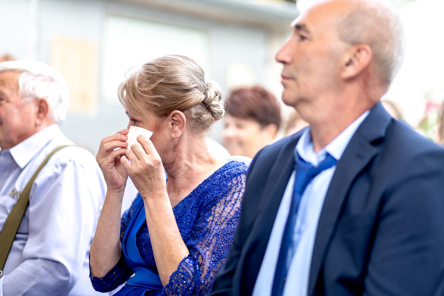 A woman in a blue dress covers her face while sitting next to a man in a business suit at an event.