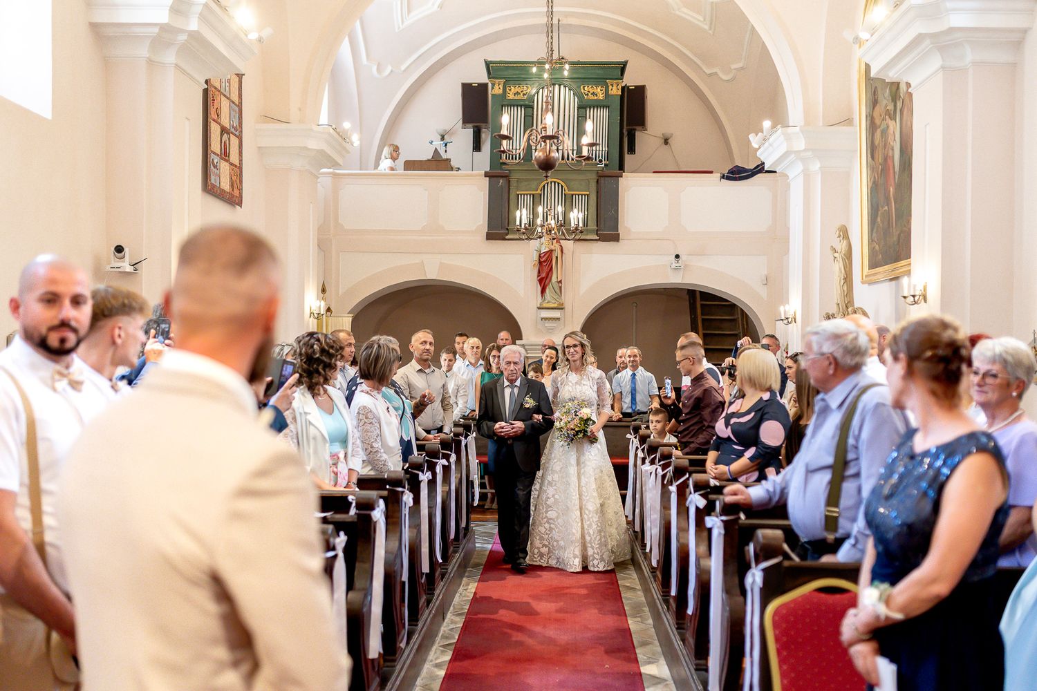 Elegant church wedding ceremony with guests seated in wooden pews and red carpet aisle under ornate arches.