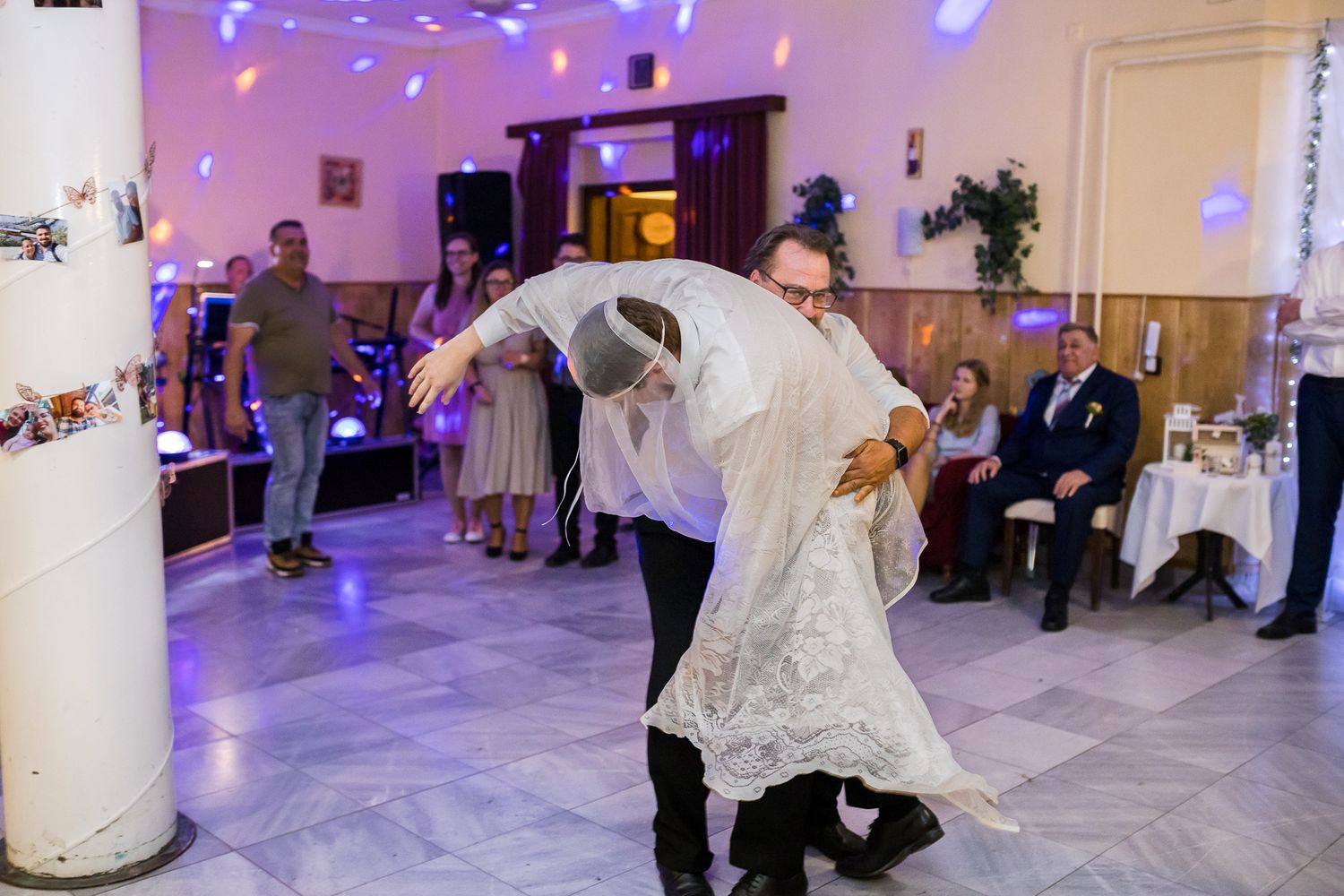A couple performs a dramatic dip during their first dance at a wedding reception with purple lighting and guests watching.