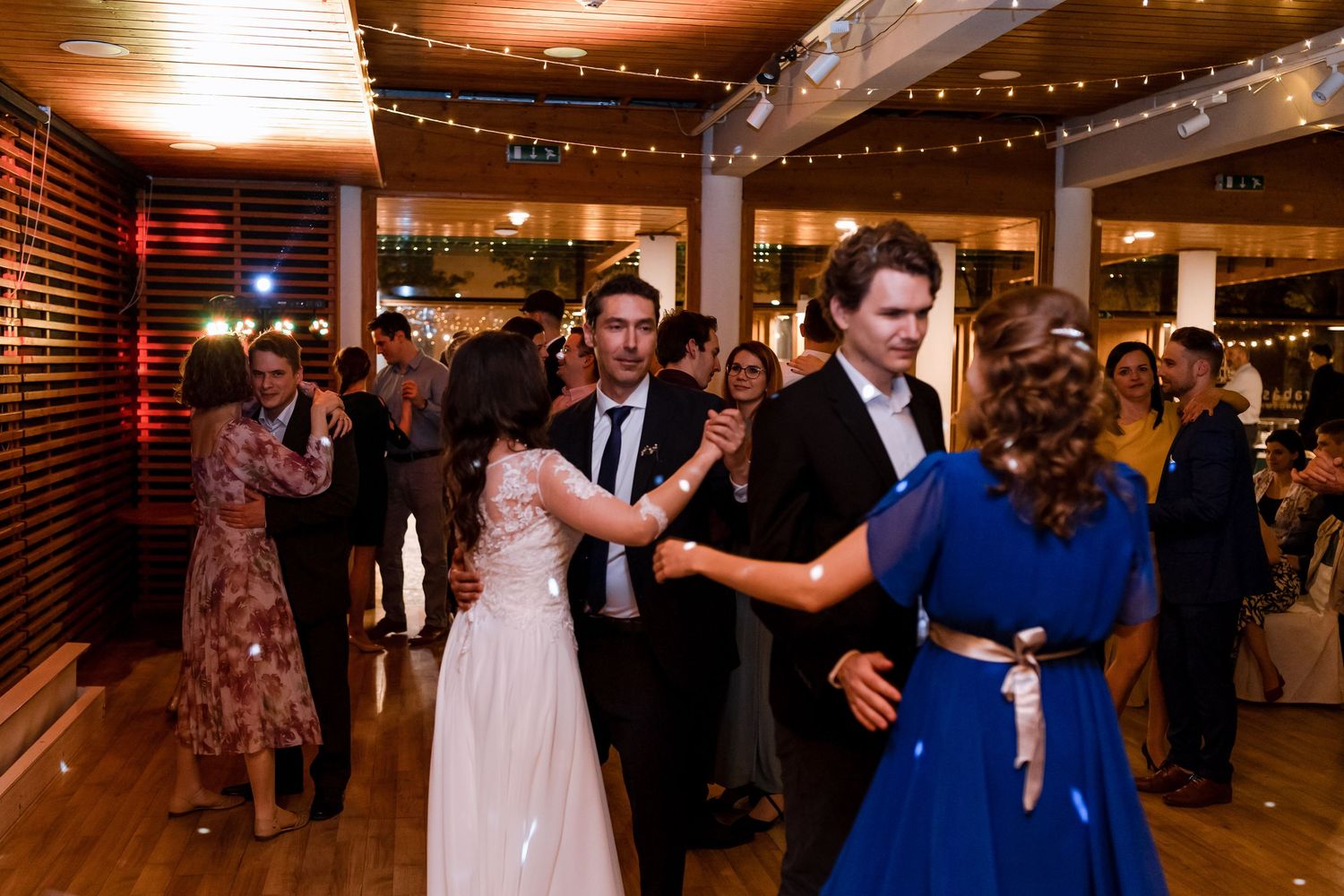 Couples dancing together at a wedding reception with string lights glowing overhead in a dimly lit venue.