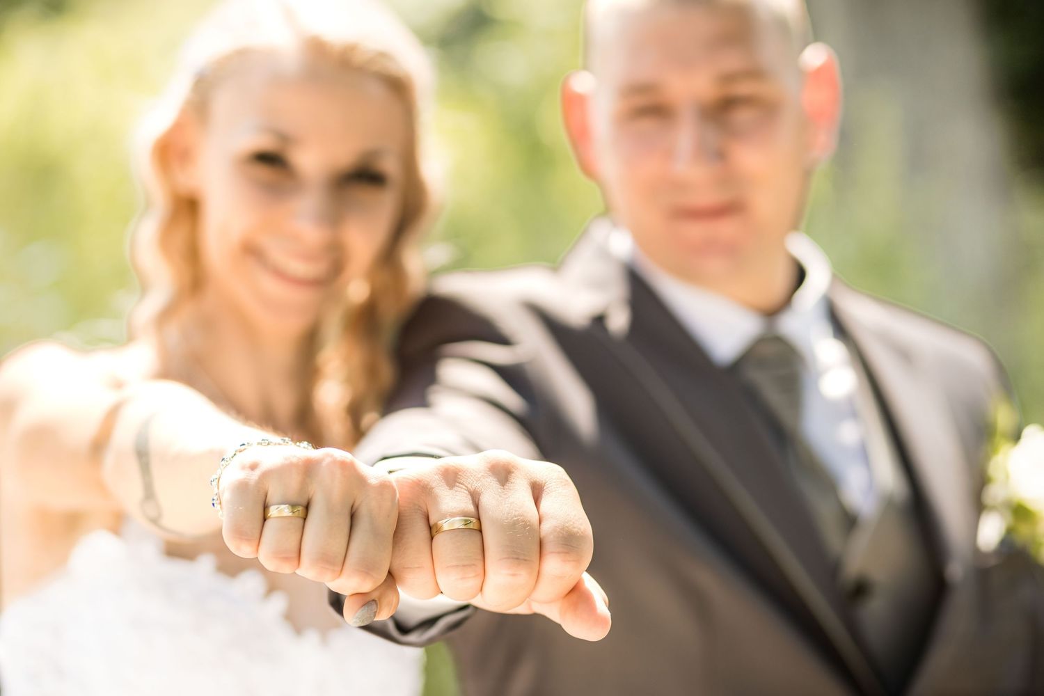 A group of people standing together outdoors holding up their hands to show their wedding rings.