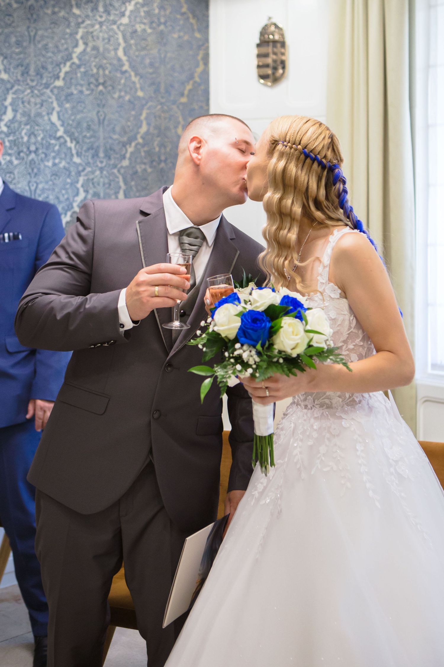 Newlywed couple shares romantic champagne toast at elegant wedding reception with blue and white floral decor.