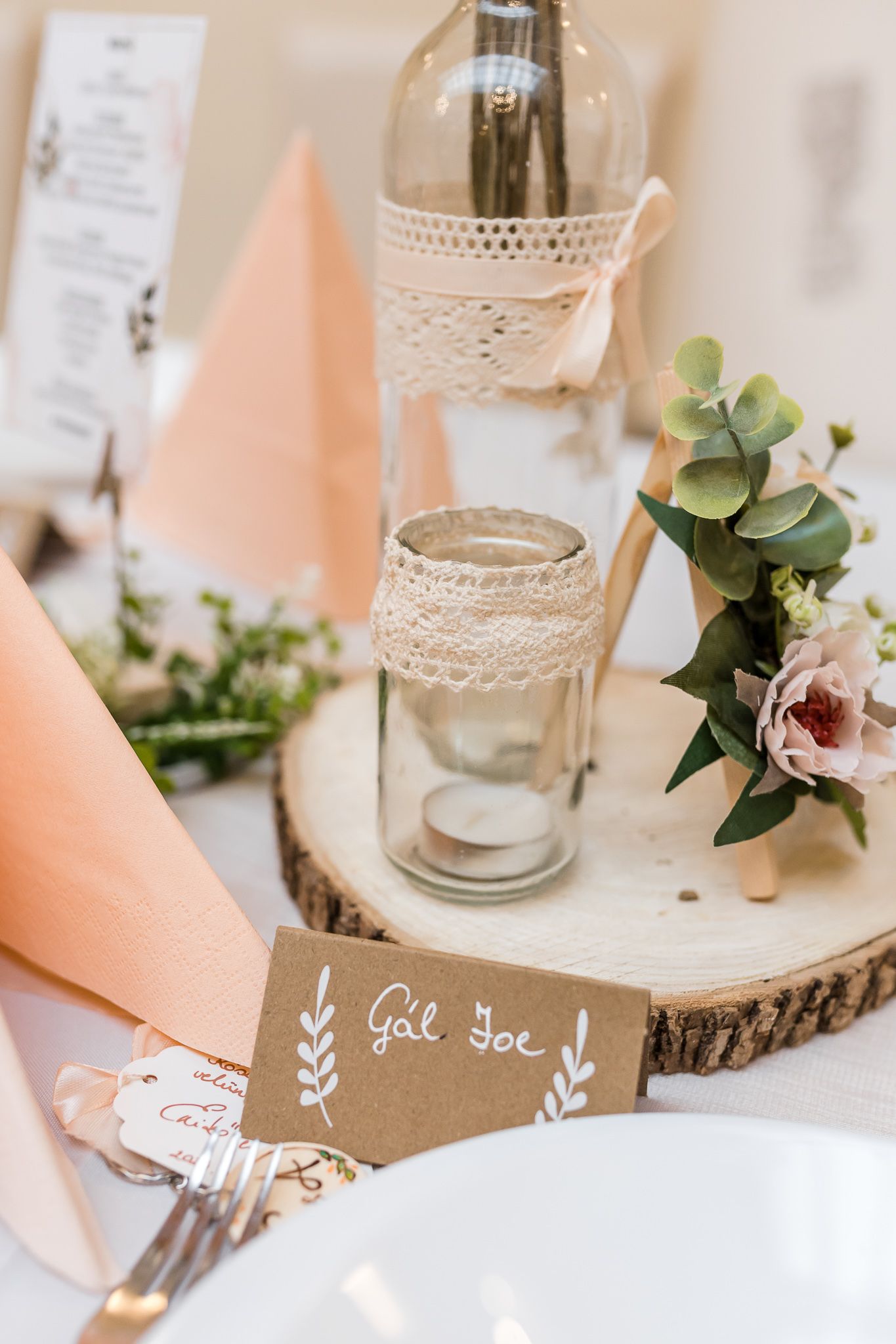 Rustic wedding table decor with wood slices, lace-wrapped candle holders, and peach napkins arranged elegantly.