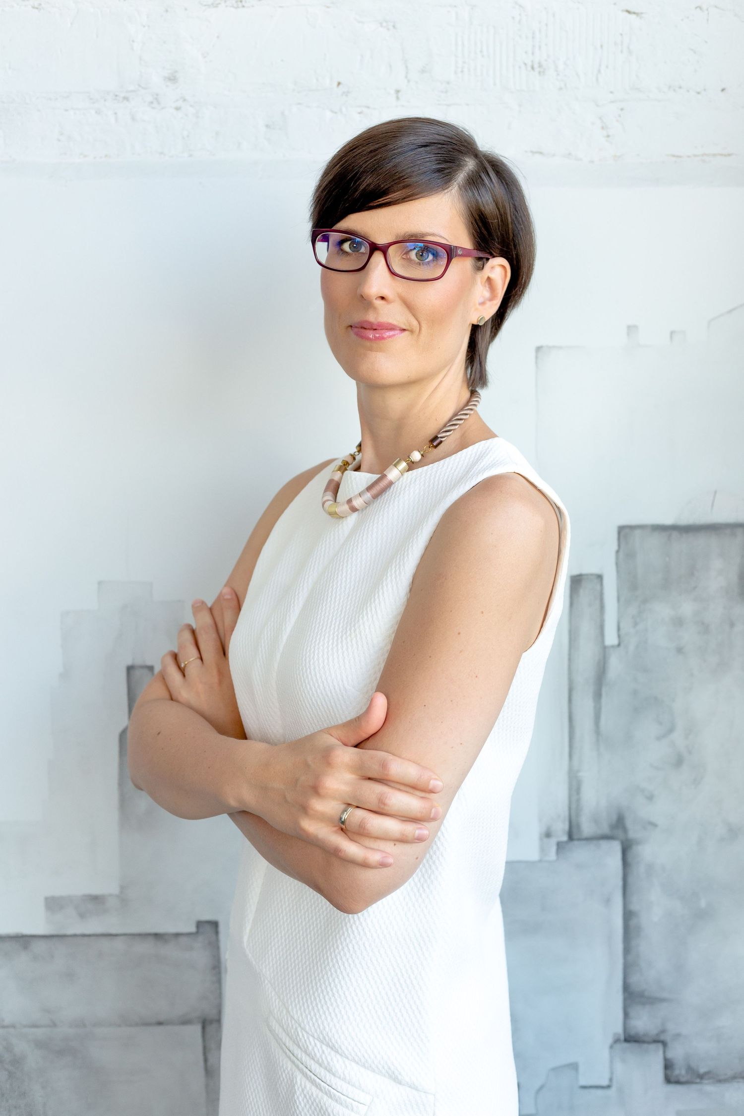 Business portrait in white sleeveless top against industrial white wall background.