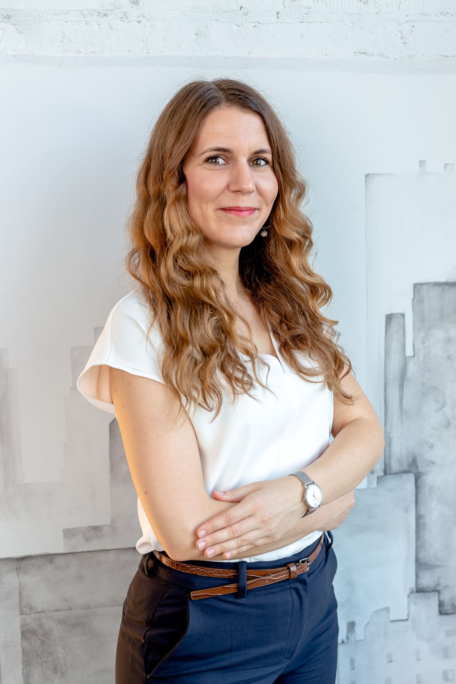 Professional portraits with wavy hair wearing white blouse and navy pants against abstract wall art.