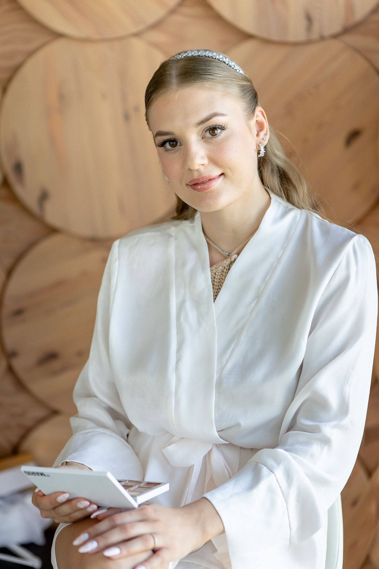 Person in white robe holding phone against wooden wall background.