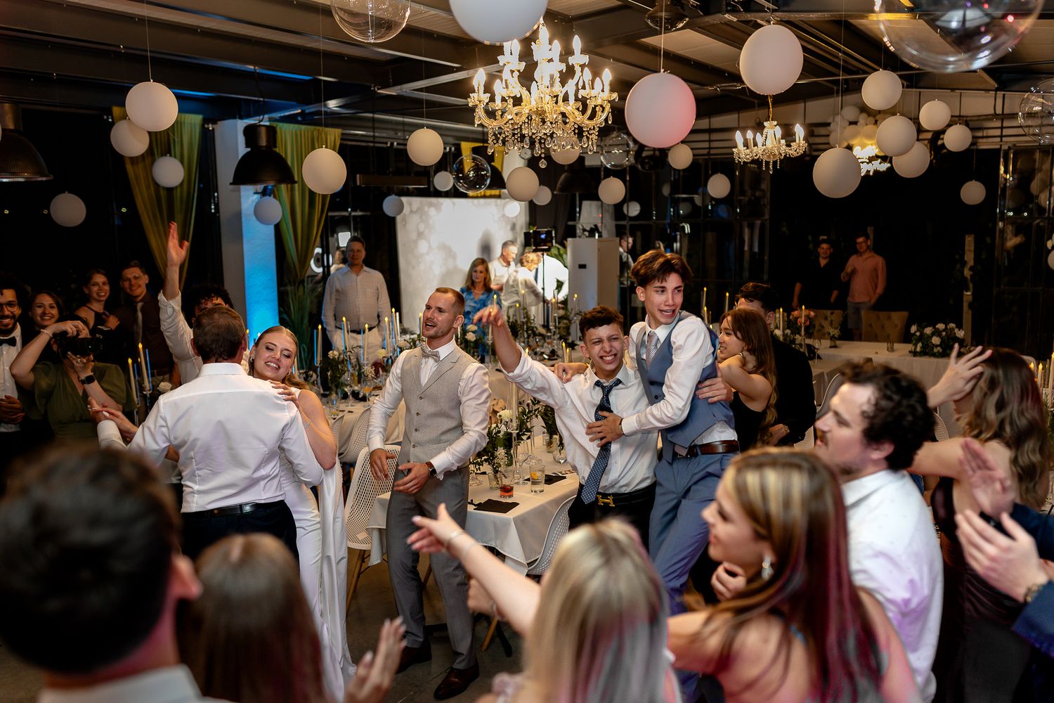 Wedding celebration in full swing with paper lanterns and crystal chandeliers overhead.