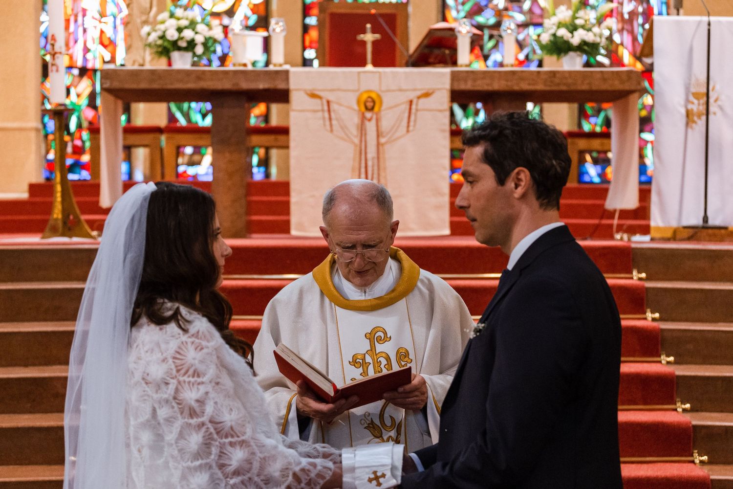 A wedding ceremony taking place at the altar of a traditional church with floral decorations and religious symbols.